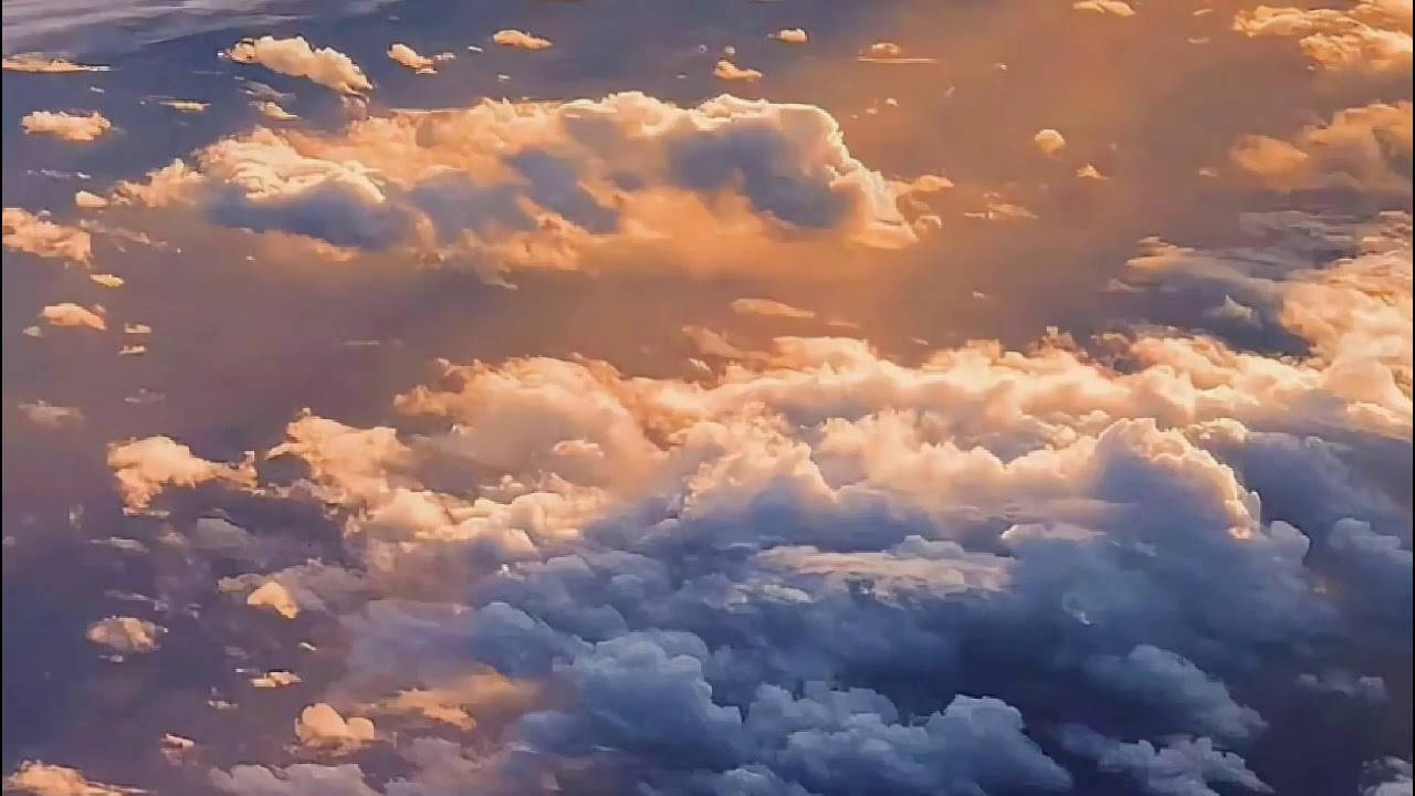 陽光雲朵美學 壁紙 — 廣闊的雲景沐浴在金色夕陽下，帶有柔和的粉紅色和藍色色調。