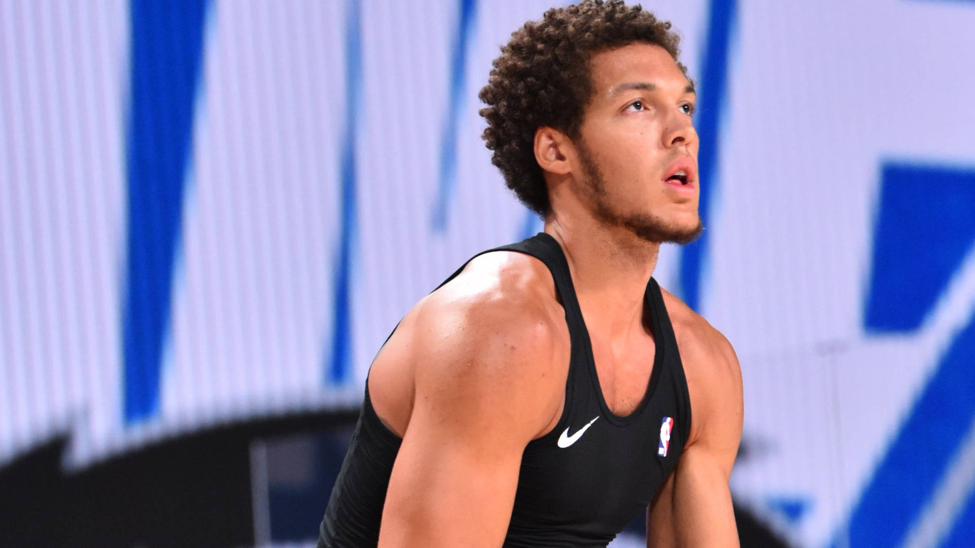 陽剛NBA阿隆·戈登 壁紙 — 一位身穿黑色球衣、專注的籃球運動員在明亮的場館燈光下，於激烈的比賽中向上看。