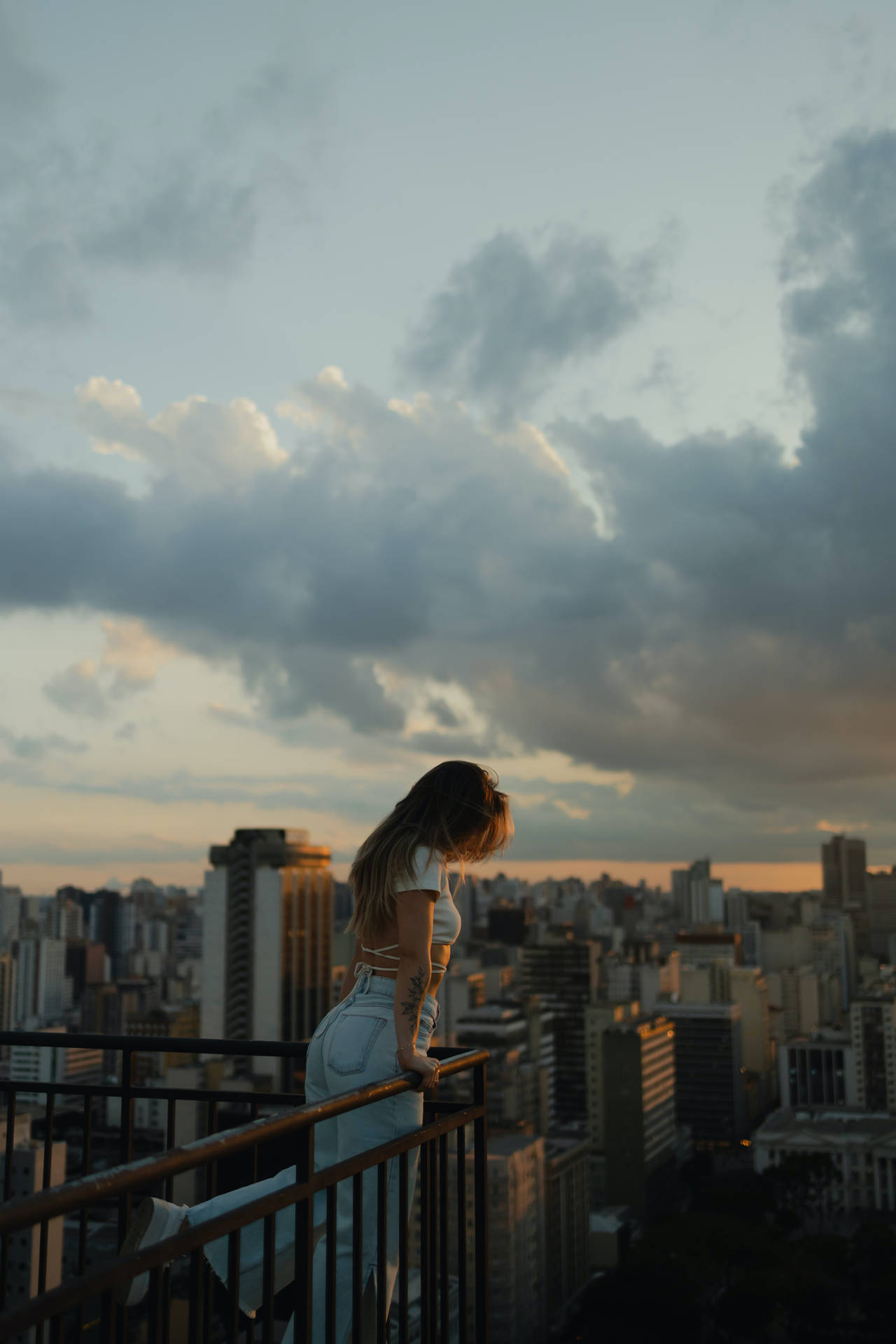 白衣女性從陽台俯瞰夕陽下的城市