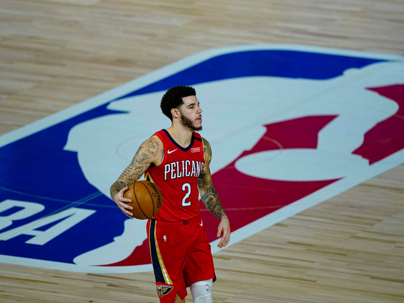 身穿紅色Pelicans球衣的籃球運動員在球場上持球。