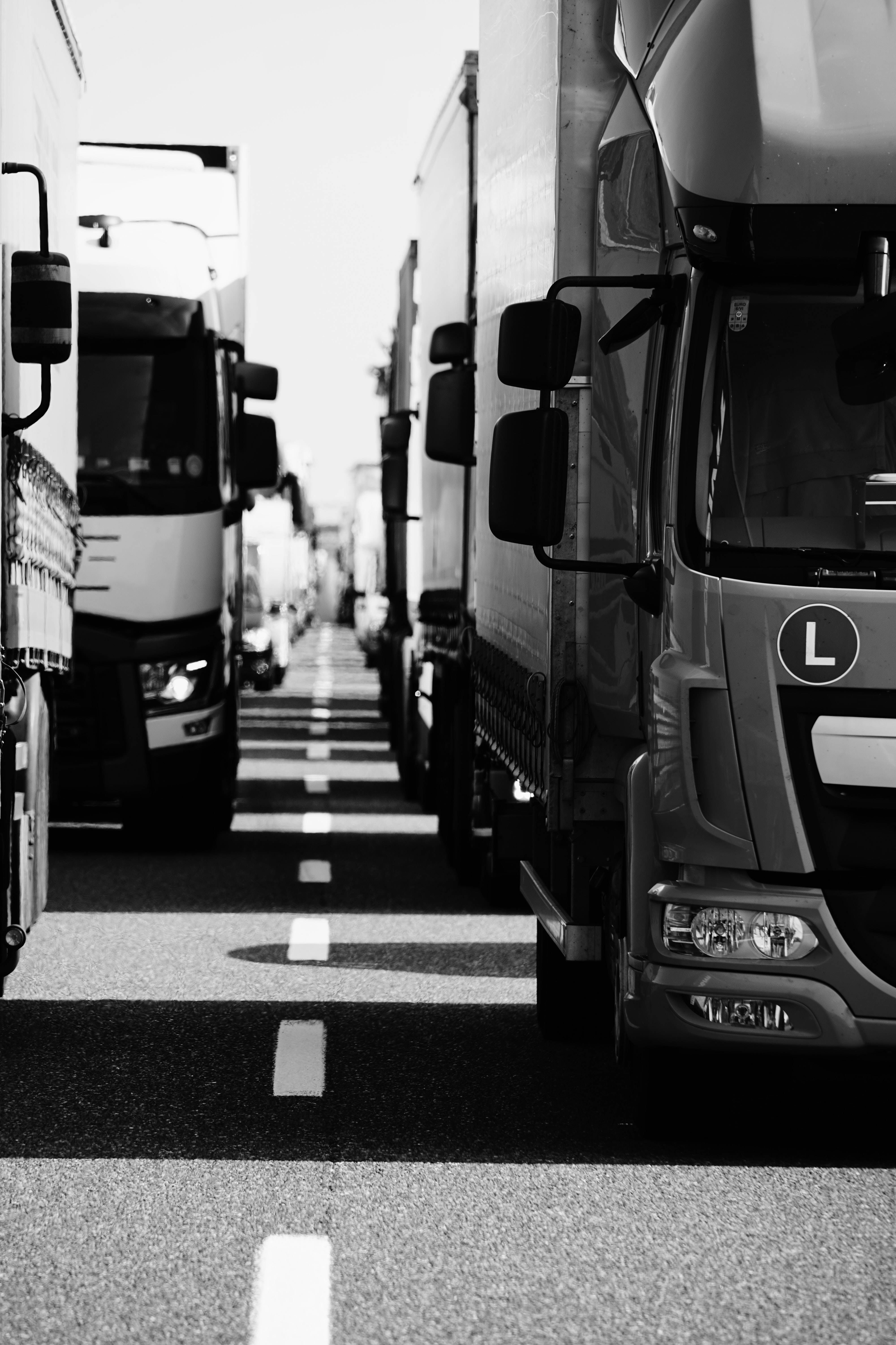 隊列中的灰階卡車 壁紙 — 一條黑白透視的道路，兩旁停滿了半掛卡車，形成一條由鉻和陰影組成的隧道。