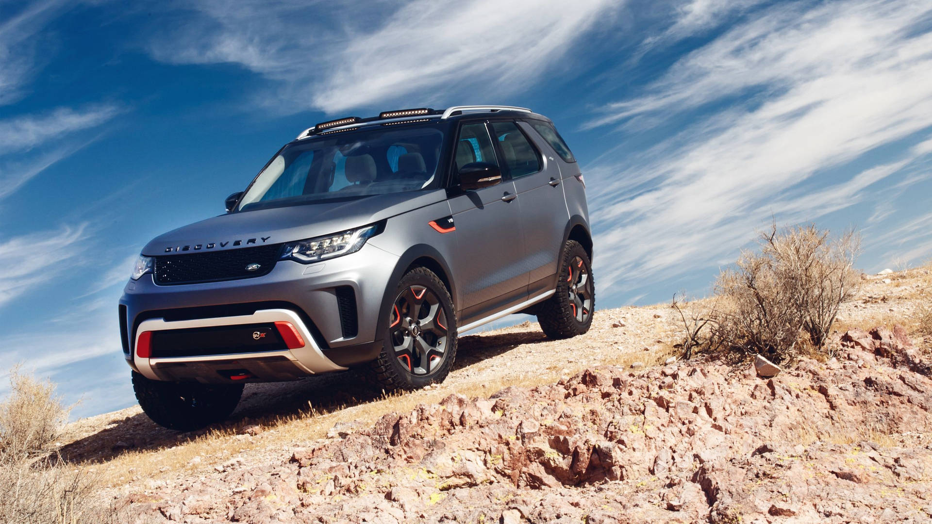 銀色 Land Rover Discovery 在黃昏時攀爬岩石沙漠山丘。