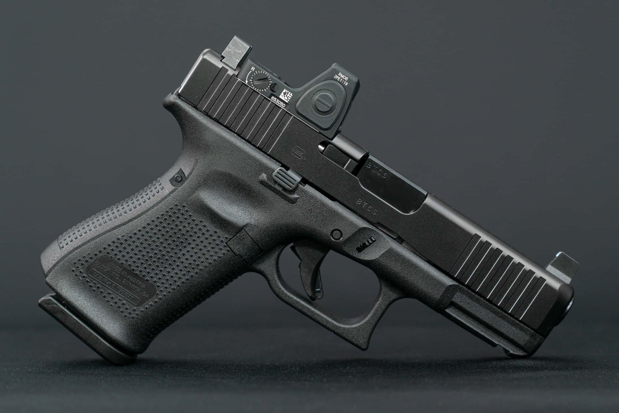 隨時待命 —— Glock 19 壁紙 — 一支帶有紅點瞄準器的時尚黑色Glock手槍，在攝影棚燈光下放置於深色表面上。