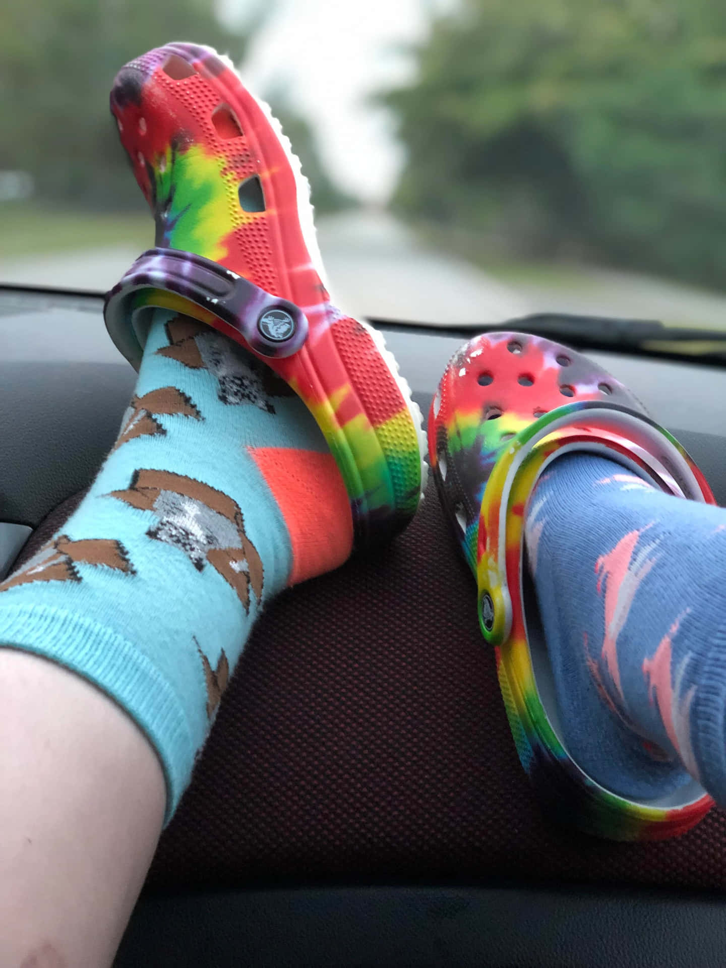 雙腳穿著彩色Crocs和圖案襪子，擱在汽車儀表板上。
