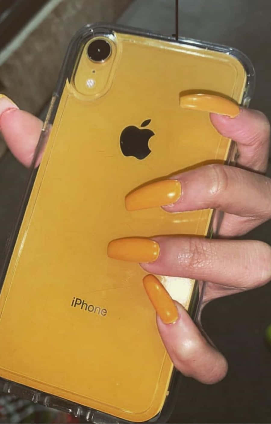 帶有橙色指甲的手拿著黃色iPhone XR。