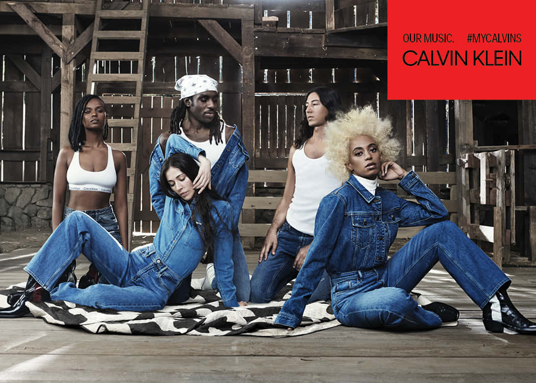 隨時隨地展現時尚風采，盡在Calvin Klein服飾 壁紙 — 五位模特兒穿著牛仔服裝，在質樸的木穀倉內的花紋毯子上自信地擺姿勢。