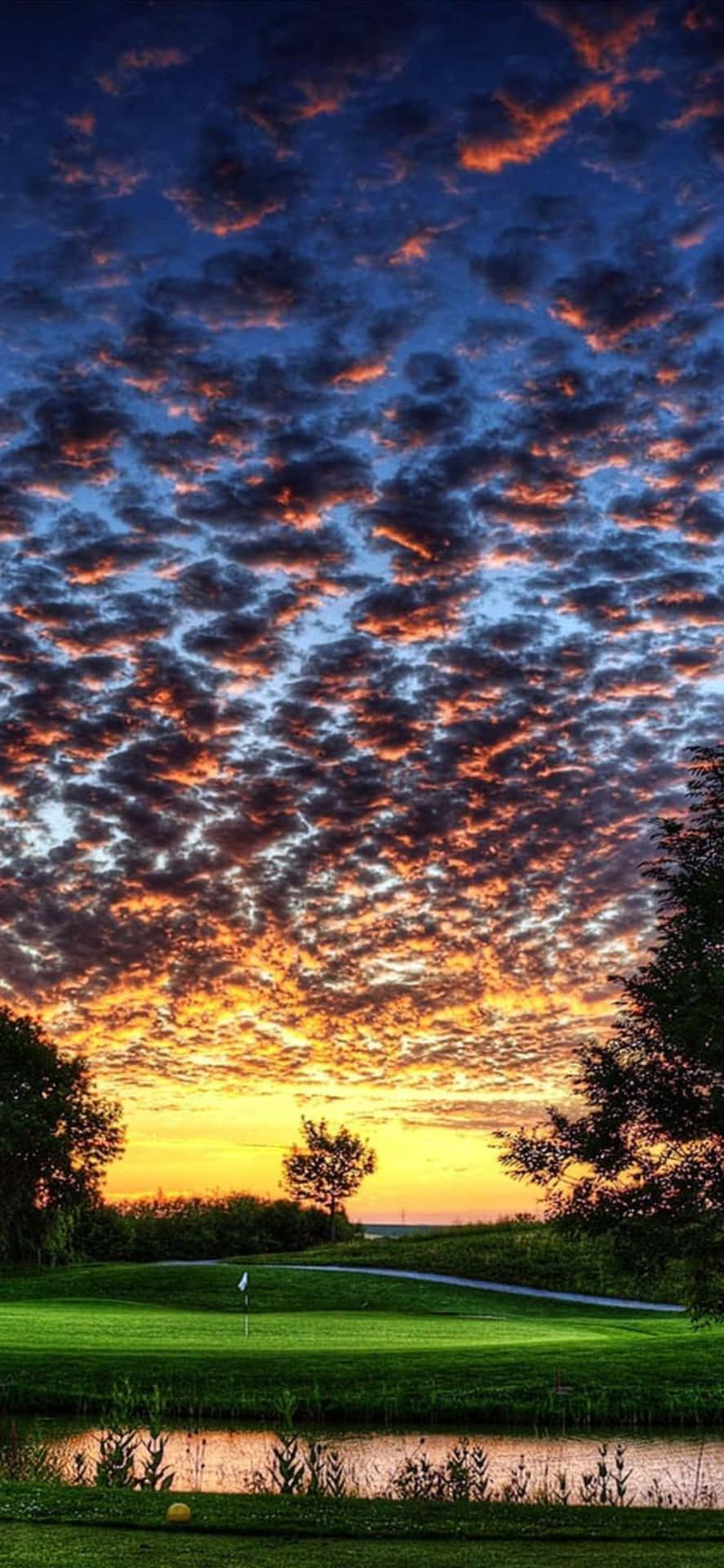 日落時分的高爾夫球場，色彩繽紛的雲彩和水障礙