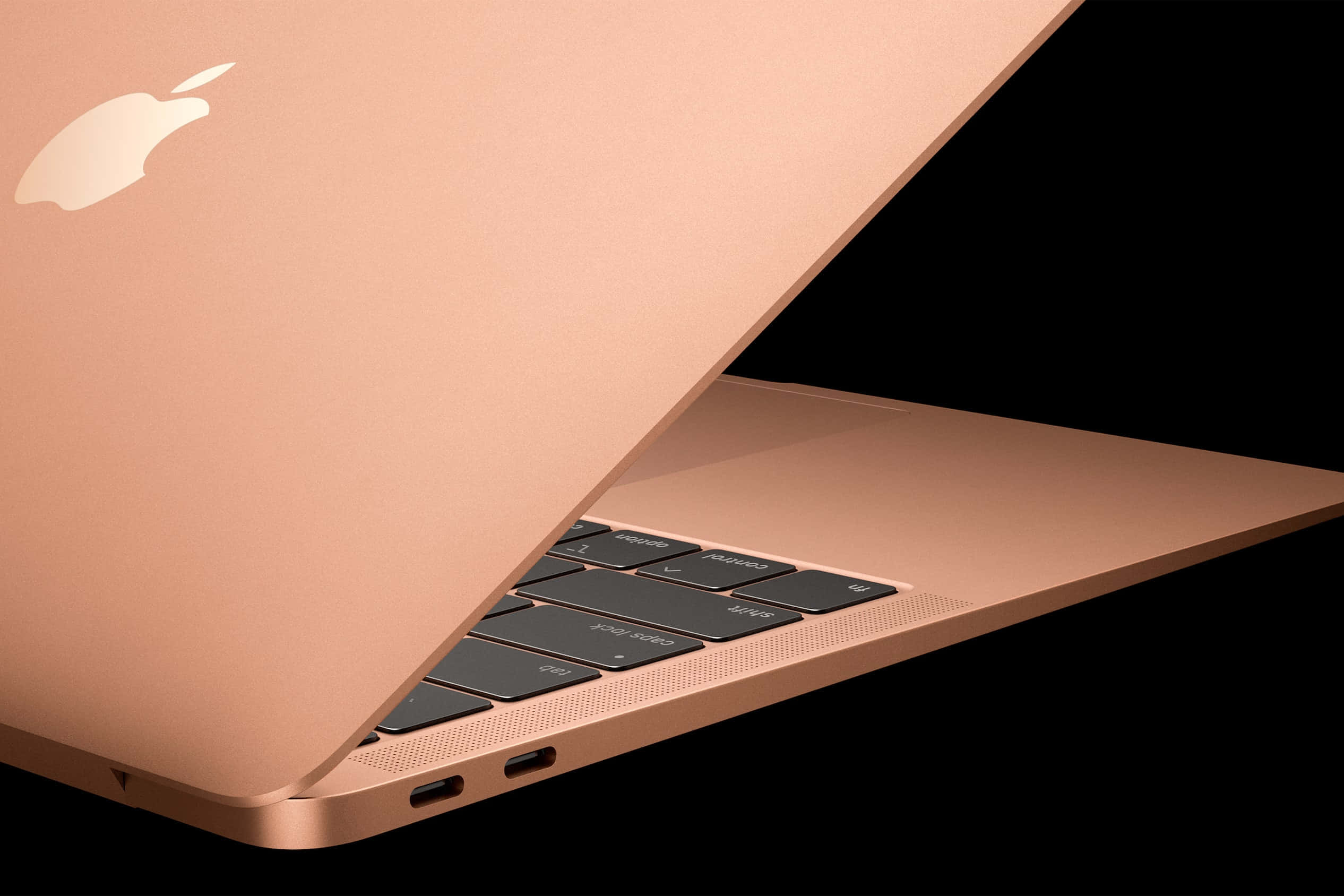隨身攜帶 Macbook，隨時享受世界 壁紙 — 一部流線型玫瑰金色 MacBook 手提電腦斜向打開，在純黑背景上展示其鍵盤和標誌。