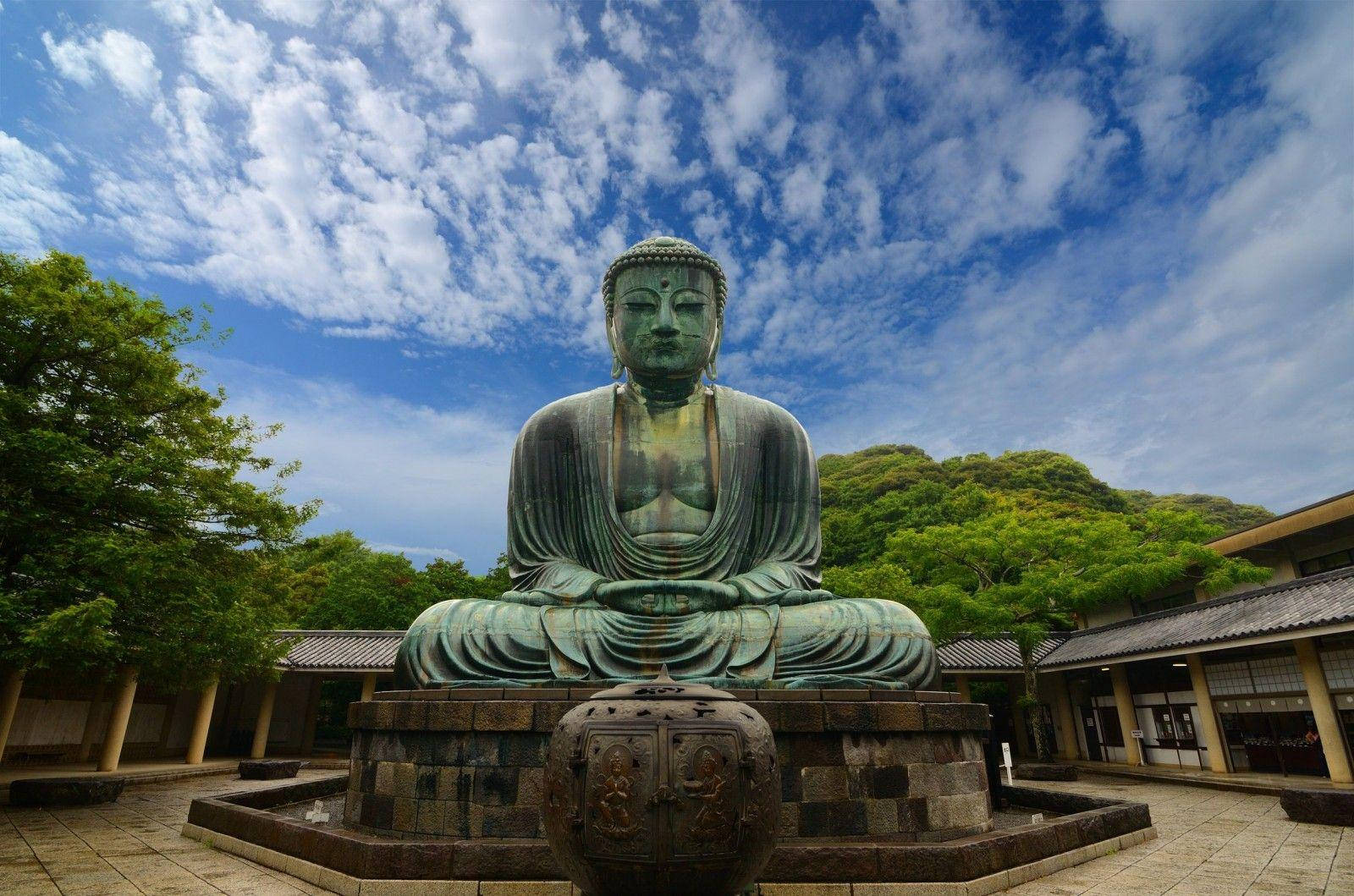 藍天白雲下寺廟庭院中的大型青銅佛像。
