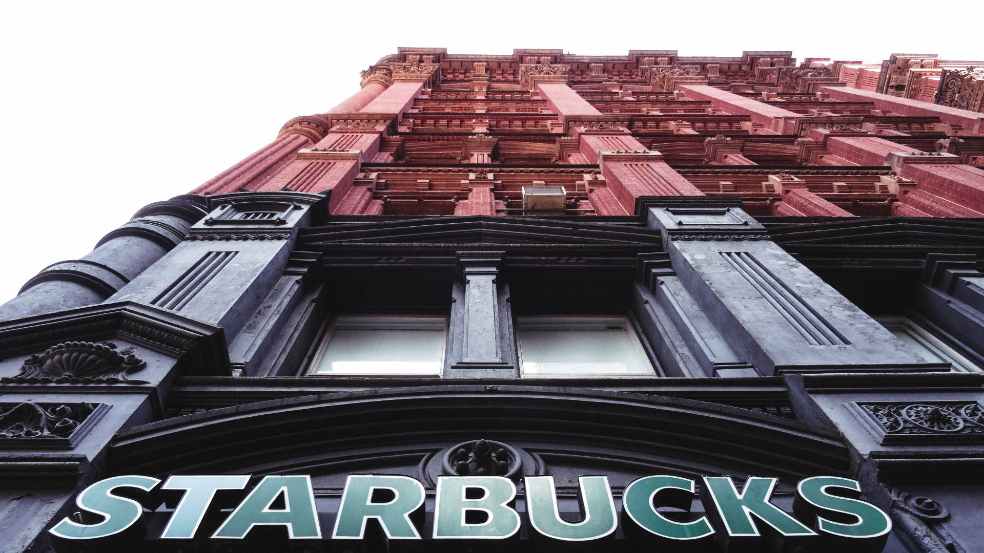 一棟紅磚建築，帶有黑色飾邊和街邊的Starbucks招牌。 — 星巴克 壁紙