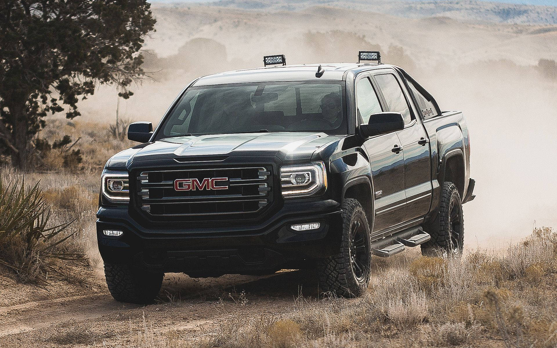 雄偉的 GMC SIERRA 行駛於高速公路 壁紙 — 一輛黑色GMC Sierra皮卡車在乾燥的沙漠景觀中行駛，揚起灰塵，植被稀疏。