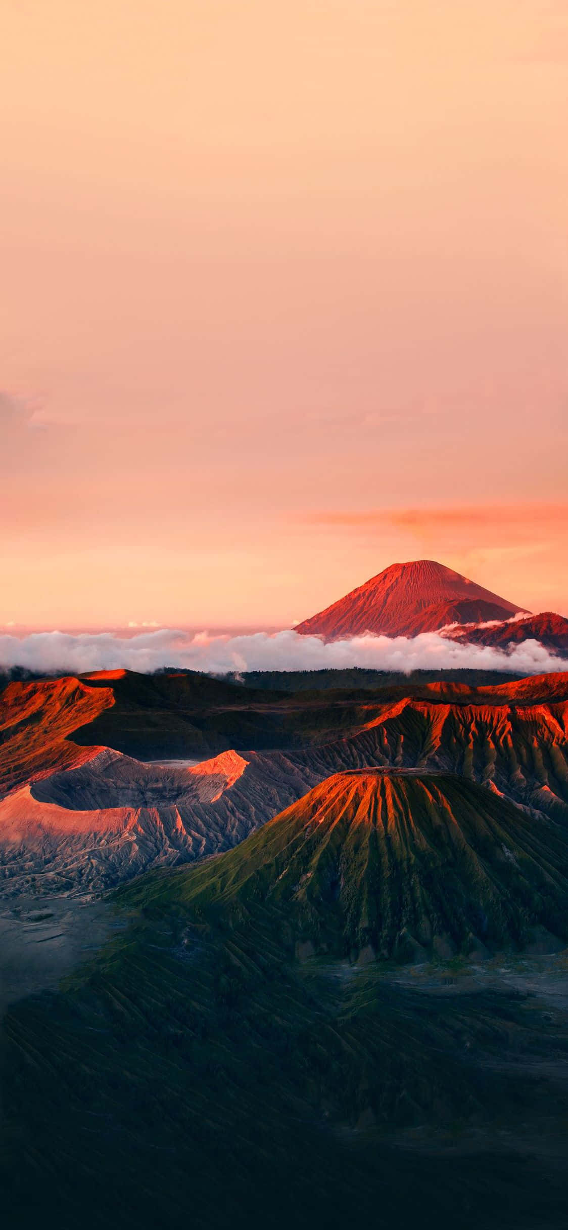 Minimalist Phone 桌布 壁紙 — 雄偉的火山山峰聳立在沐浴在溫暖粉紅和橙色日出光線中的雲層之上。