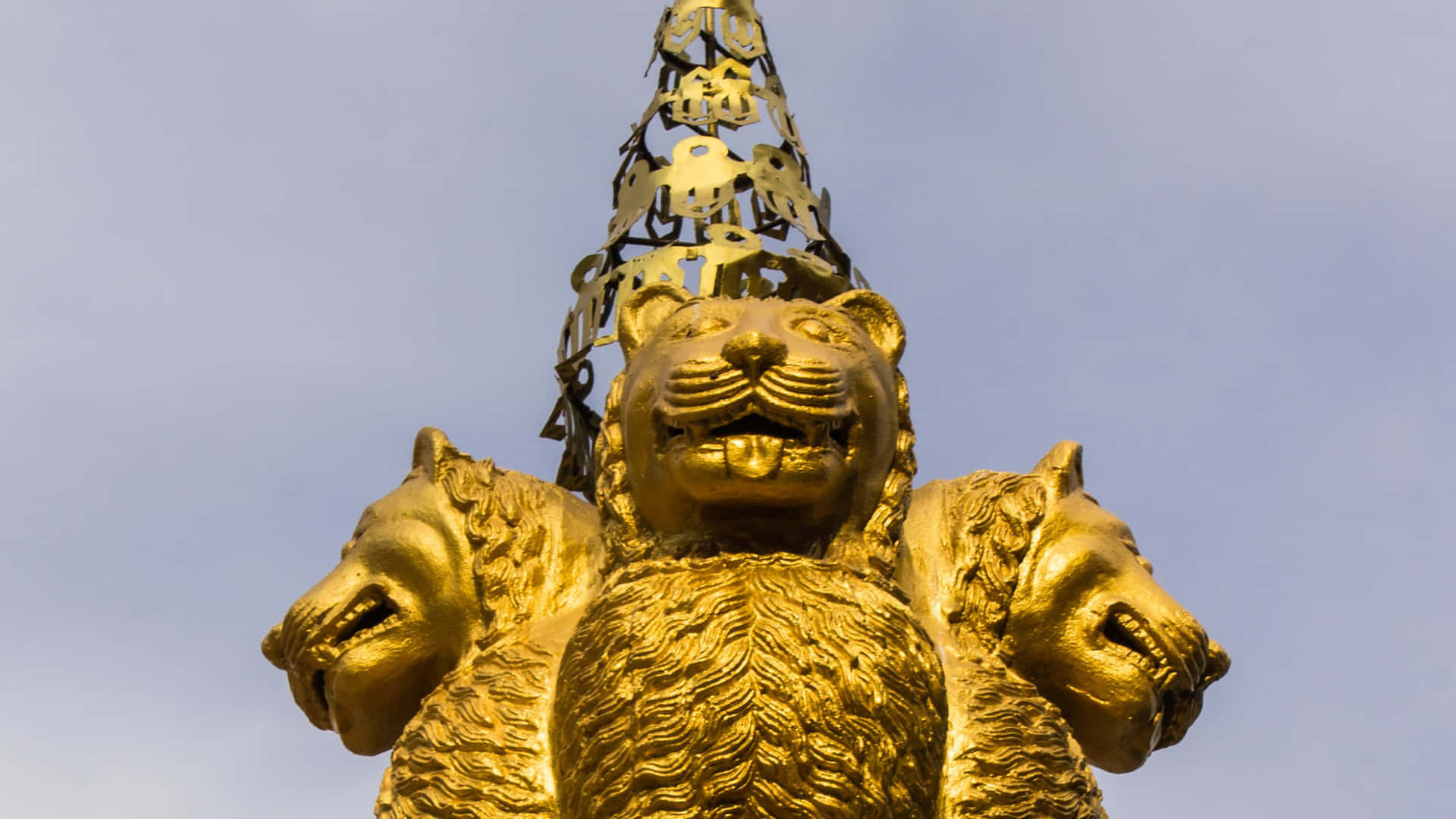 金色三頭獅子雕像，戴著王冠，襯以藍天。