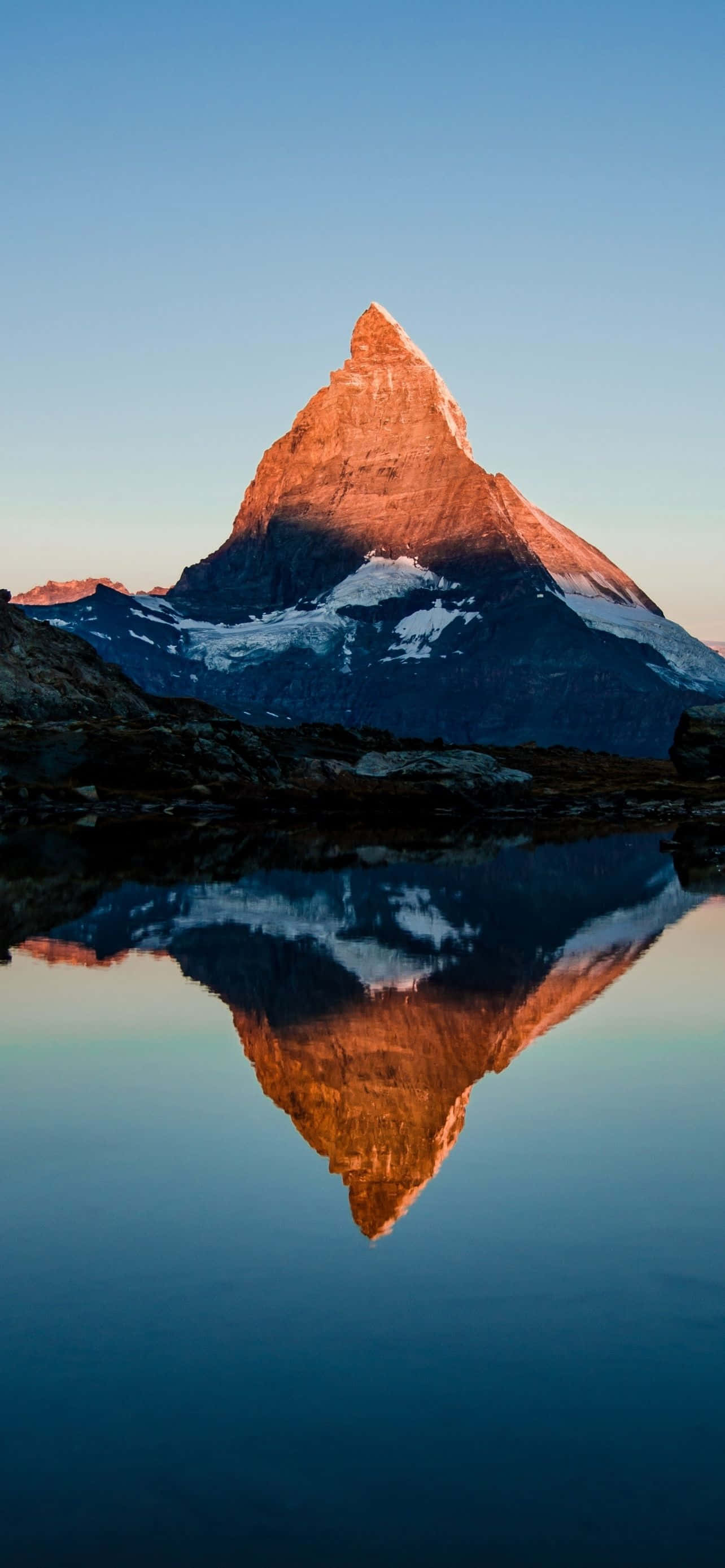 Mountain iPhone 桌布 壁紙 — 雄偉的雪山頂在金色日出光芒中閃耀，完美倒映在下方平靜的高山湖泊中。