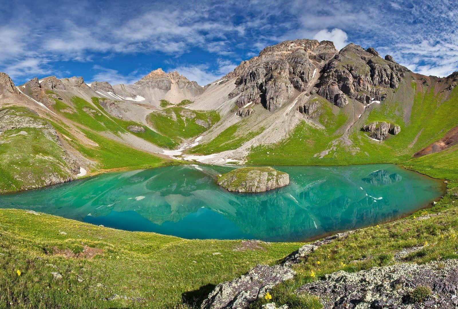 藍天下，碧綠色的山湖被綠色山坡和岩石山峰環繞。