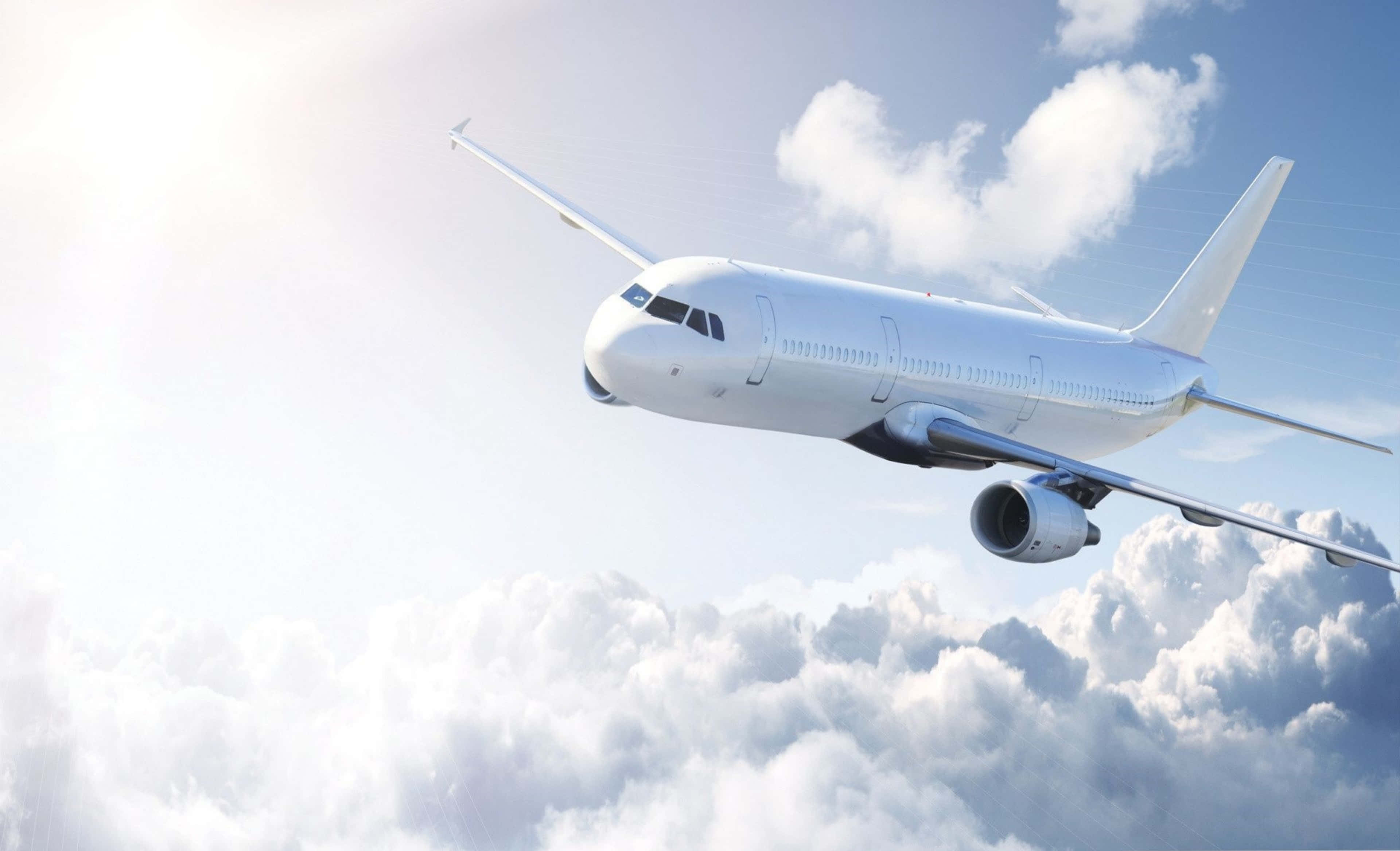 雄偉飛機翱翔高空 4K超高清 壁紙 — 一架流線型白色客機在明亮的藍天下優雅地翱翔於蓬鬆的白雲之上。