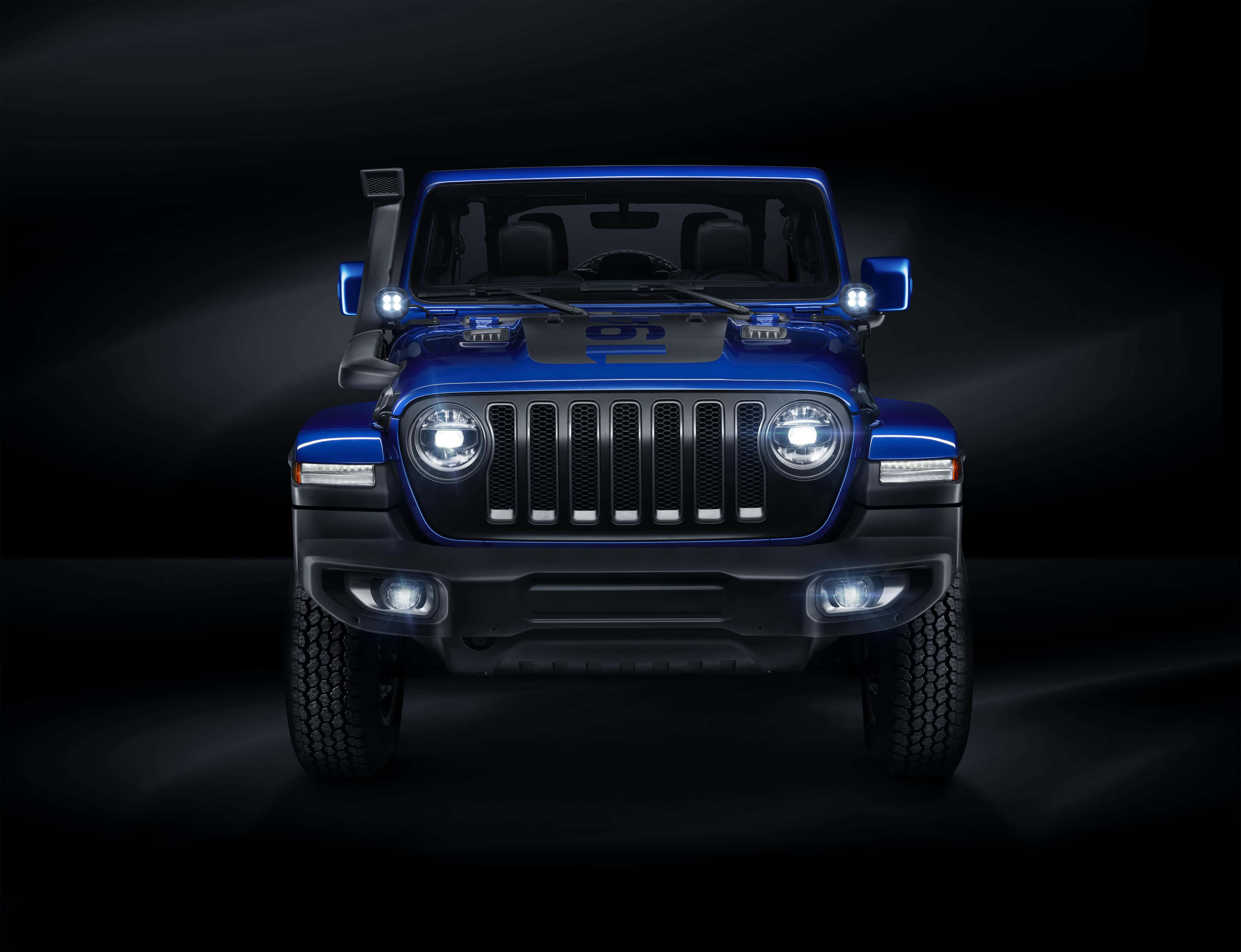 雄渾吉普自由光征服崎嶇山野 壁紙 — 一輛引人注目的藍色Jeep Wrangler在黑暗的攝影棚環境中，車頭燈閃耀，向黑色背景投射出戲劇性的光束。