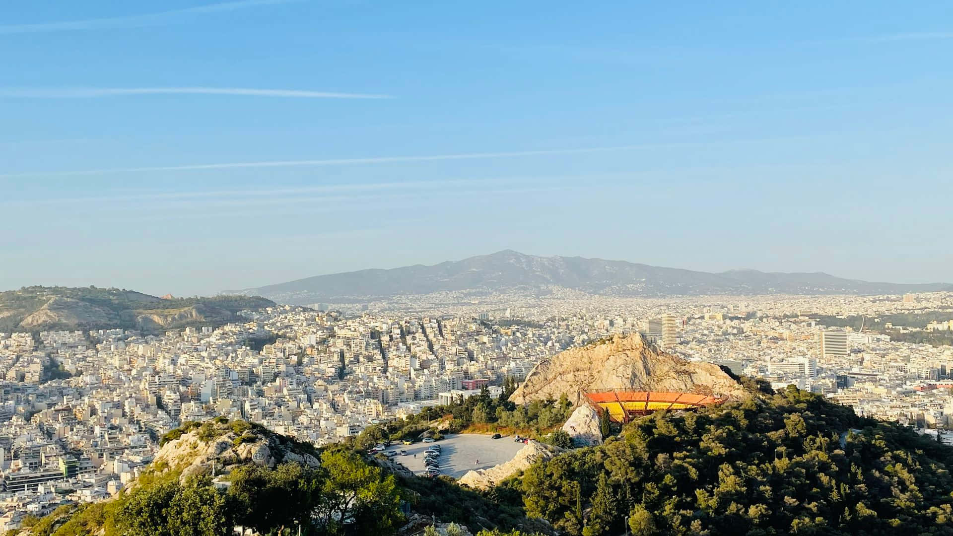 雅典利卡貝圖斯山劇場壁紙 壁紙 — 雅典城市景觀全景，包括衛城山和古代遺址，在晴朗的藍天下。