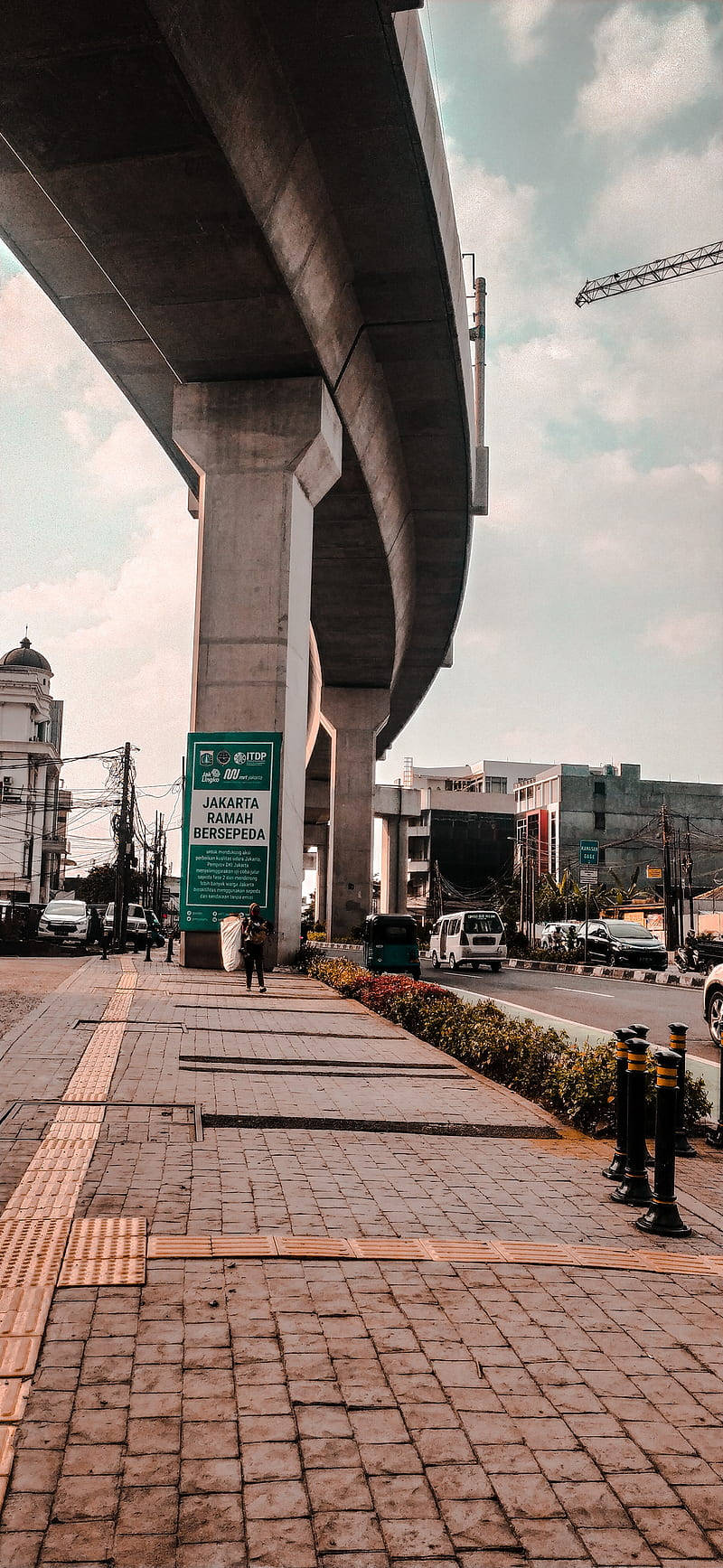 雅加達友善自行車道 壁紙 — 從低角度觀看巨型混凝土天橋下的城市街道景觀，設有行人路和遠處的城市建築。