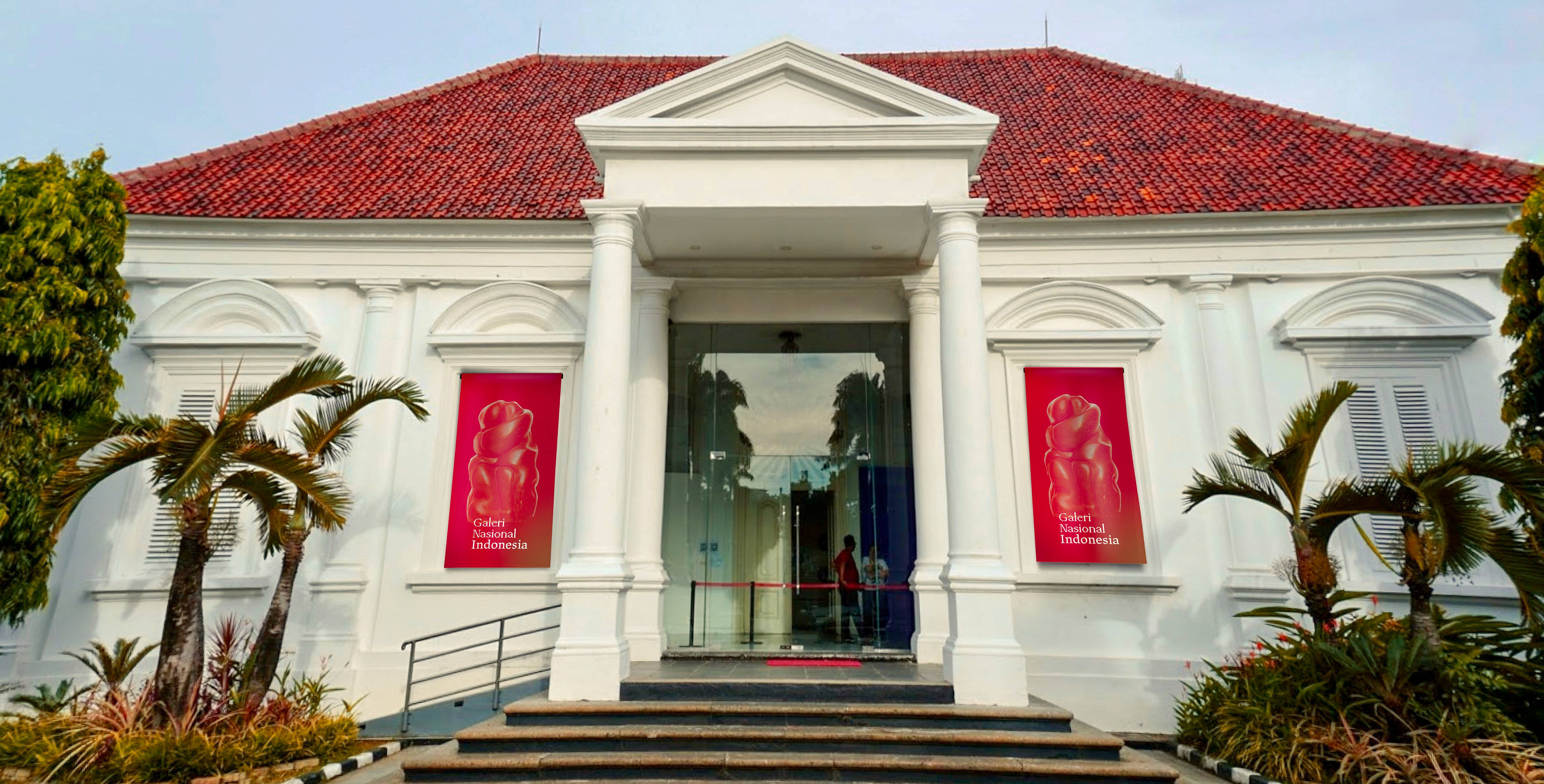 雅加達國家美術館 壁紙 — 一座大型白色殖民風格建築，擁有紅色瓦片屋頂和玻璃入口，兩旁種植棕櫚樹，天空晴朗。
