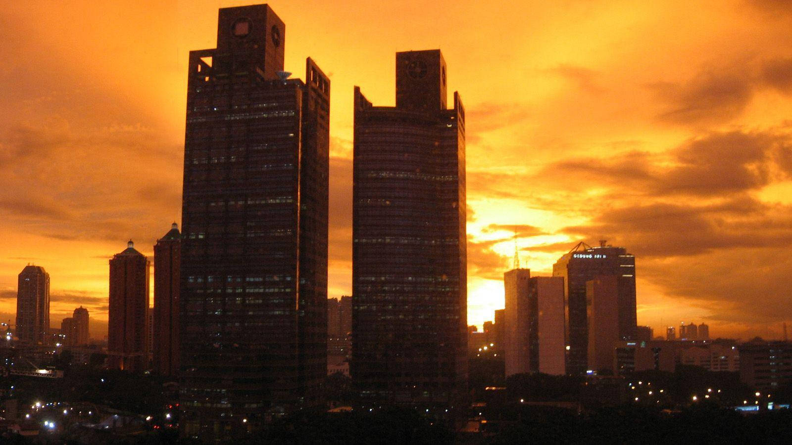 雅加達日落城市天際線 壁紙 — 高聳入雲的摩天大樓在火紅橙色的日落天空襯托下形成剪影，天空中有零星雲朵。