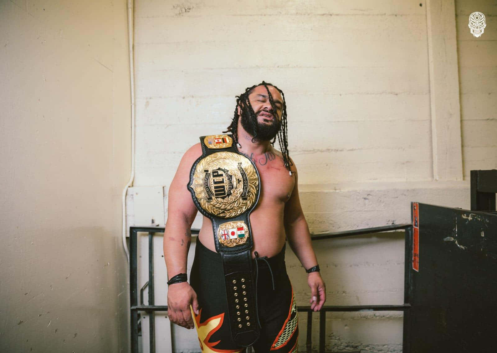雅各布·法圖 Major League Wrestling 重量級冠軍腰帶 壁紙 — 一個肌肉發達、留著辮子的摔角手自信地站在純白牆前，戴著金色冠軍腰帶。