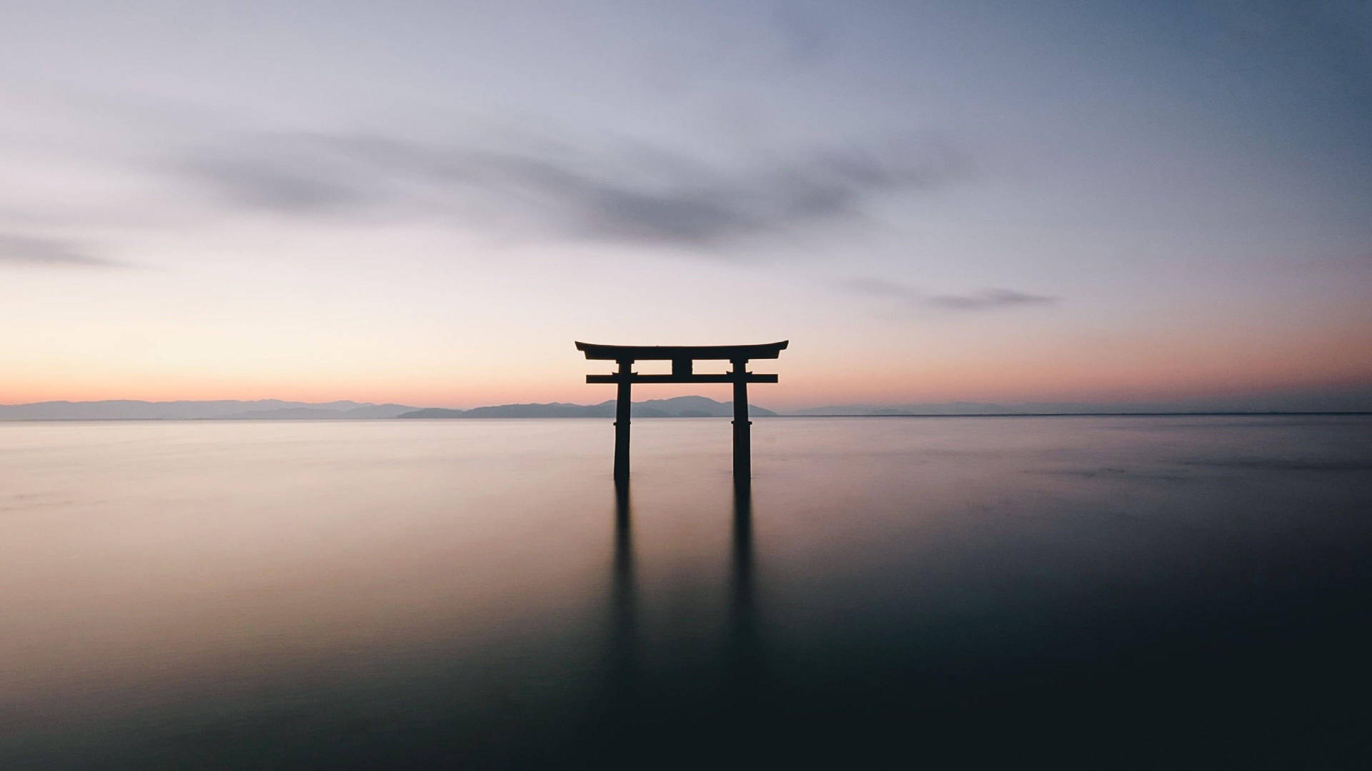 雅虎夕照鳥居 壁紙 — 一座孤獨的鳥居矗立在黃昏平靜的水面上，上方是柔和的粉紅與藍色天空。