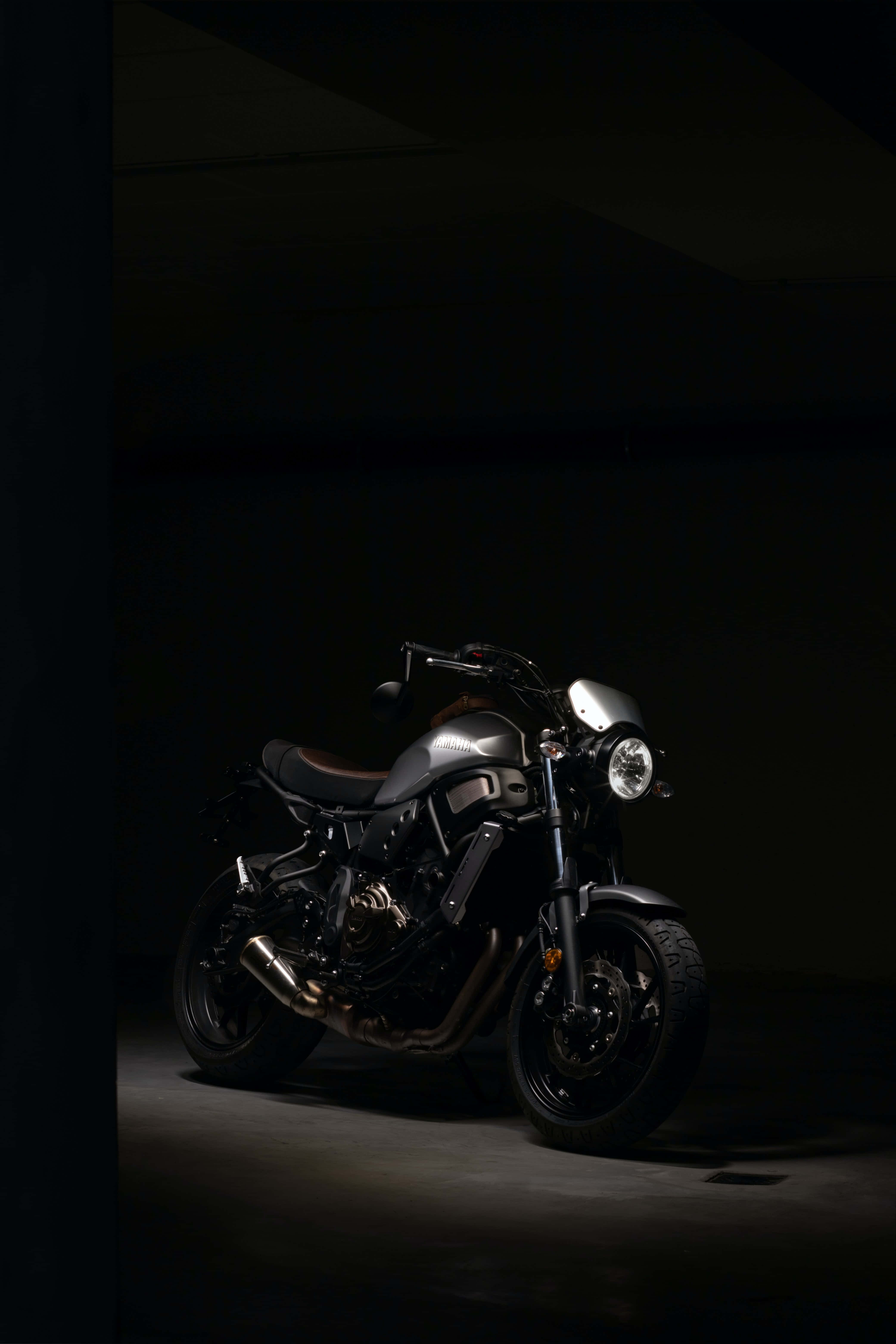 雅馬哈XSR700 —— 風格與性能的完美融合 壁紙 — 在黑暗的地下車庫中，一輛時尚的啞光黑色摩托車被單一聚光燈照亮。