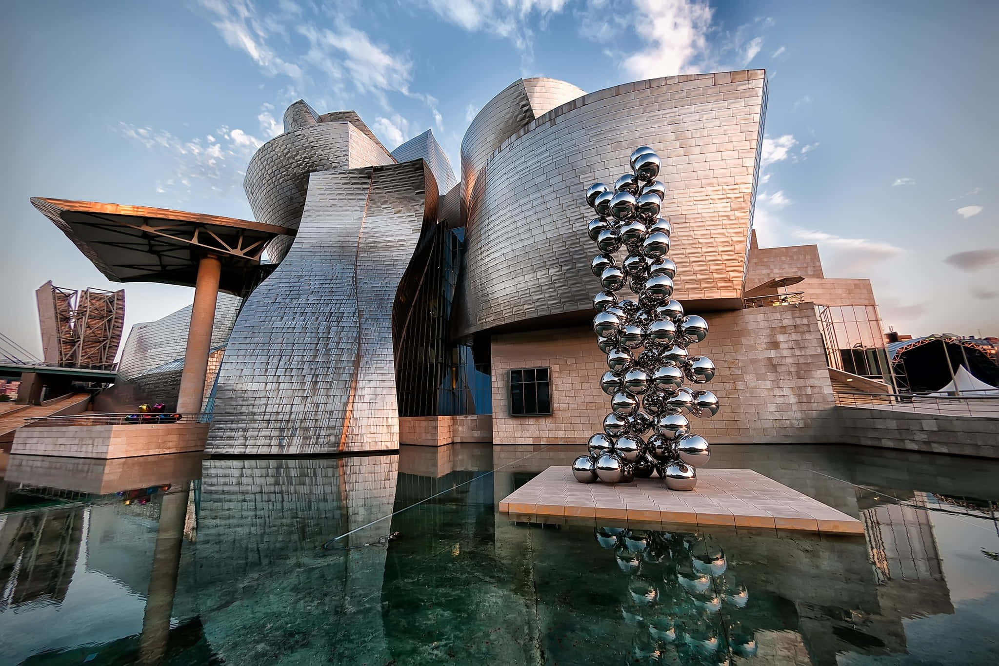 Museums 桌布 壁紙 — 雕塑般的銀色鈦金屬建築，設有反射池和鉻球雕塑，天空部分多雲。