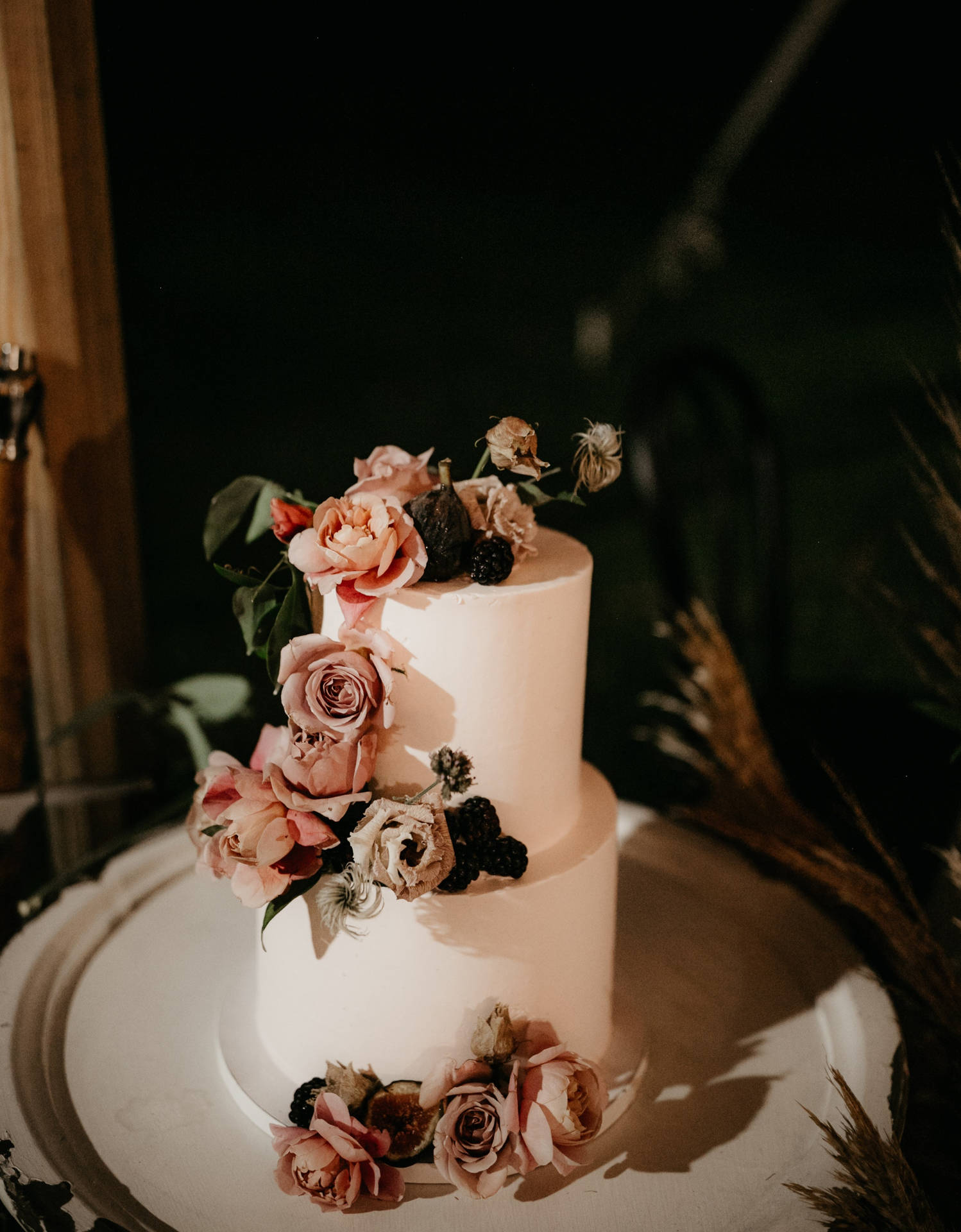 一個裝飾精美的結婚蛋糕，配有粉紅玫瑰和黑莓。