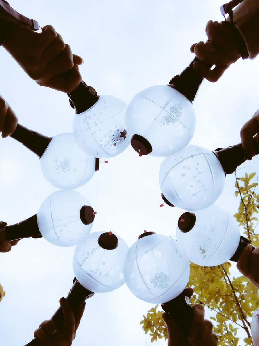 Bts Army Bomb 桌布 壁紙 — 雙手在明亮的天空下，黃葉襯托，圍成圓圈舉起發光的白色燈籠。