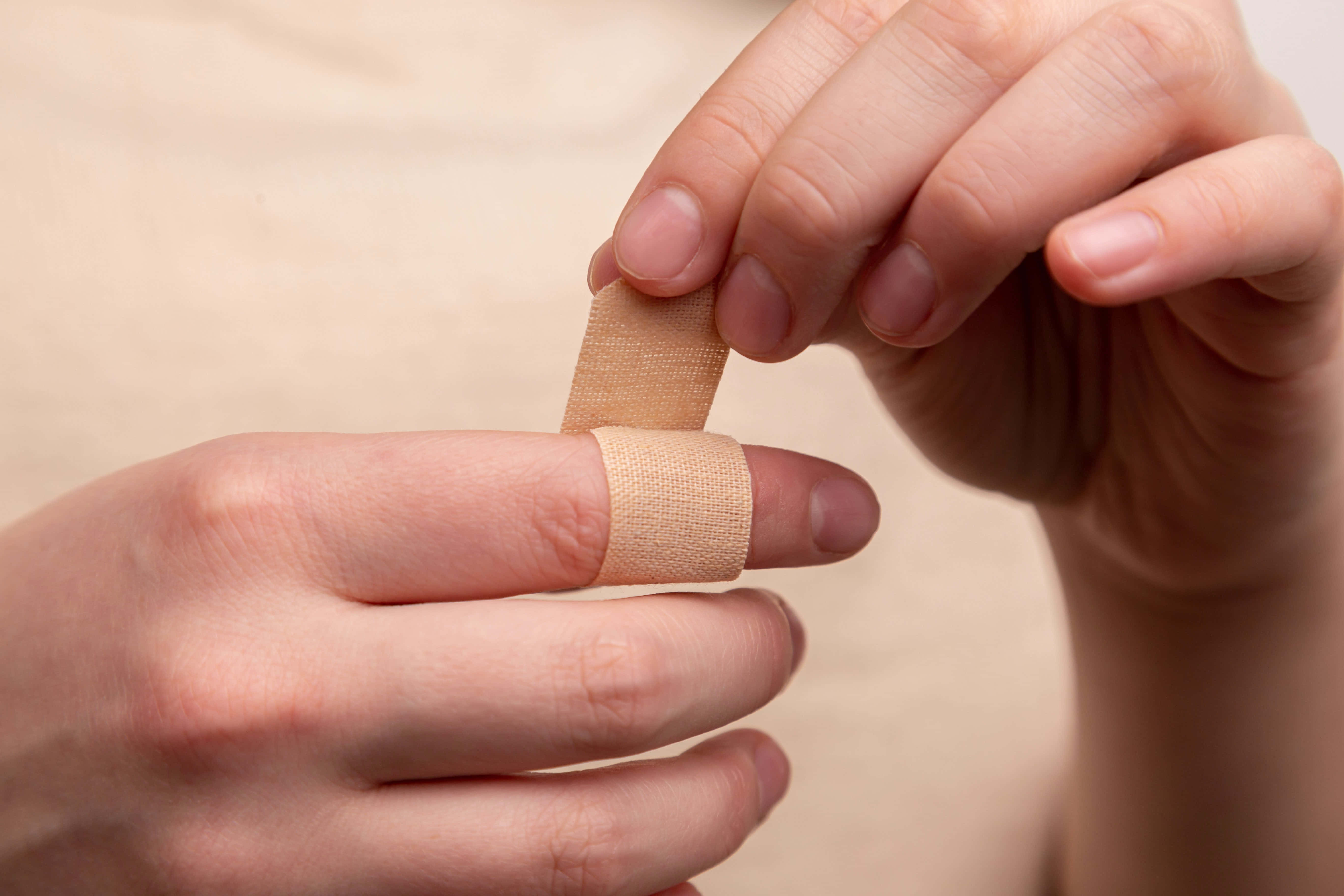 hurt 桌布 壁紙 — 雙手在柔和自然光下將米色黏性繃帶貼在手指上的特寫。