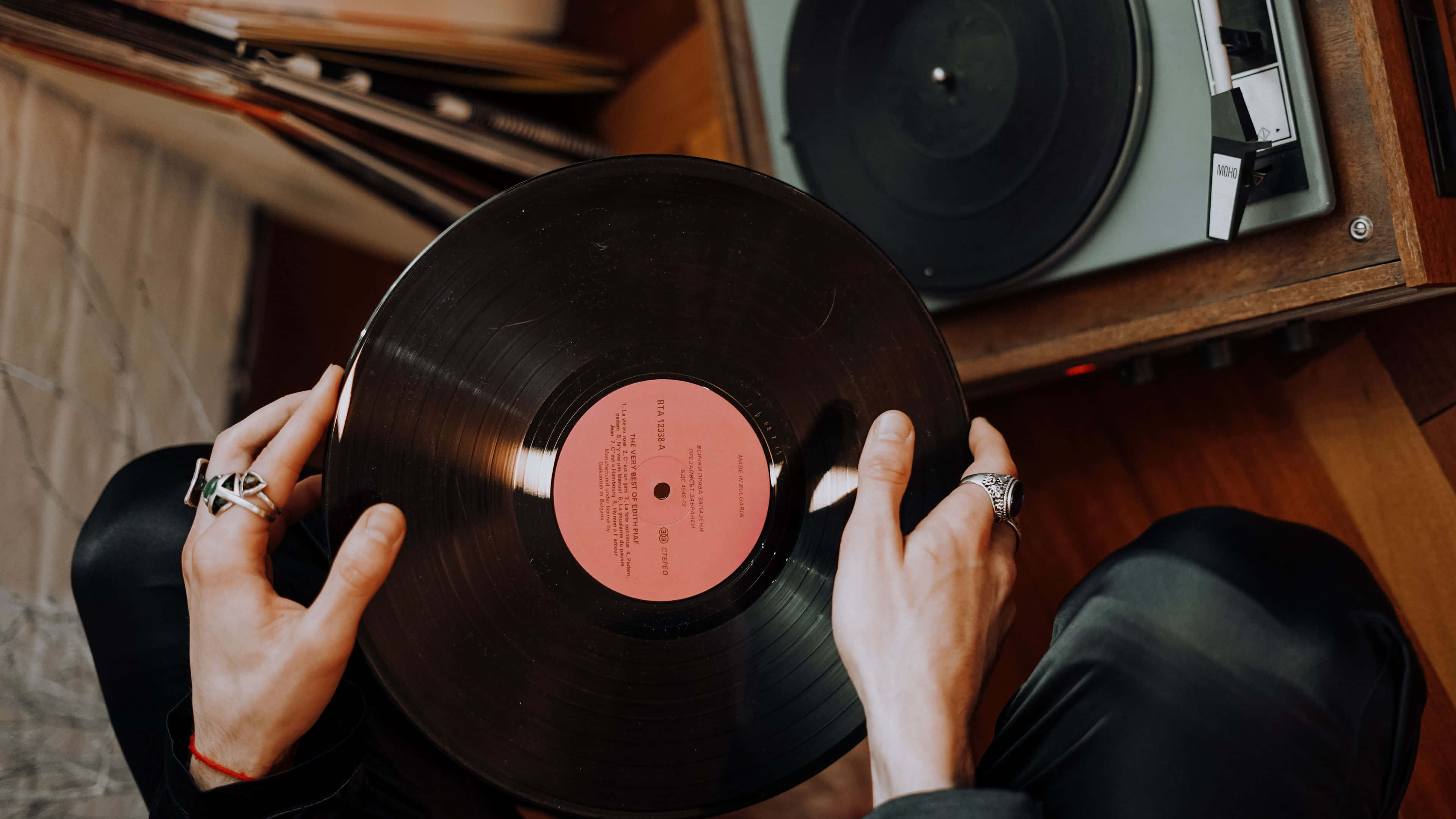 record 桌布 壁紙 — 雙手在溫暖照明的木質房間中，將黑膠唱片舉在復古唱盤上方。