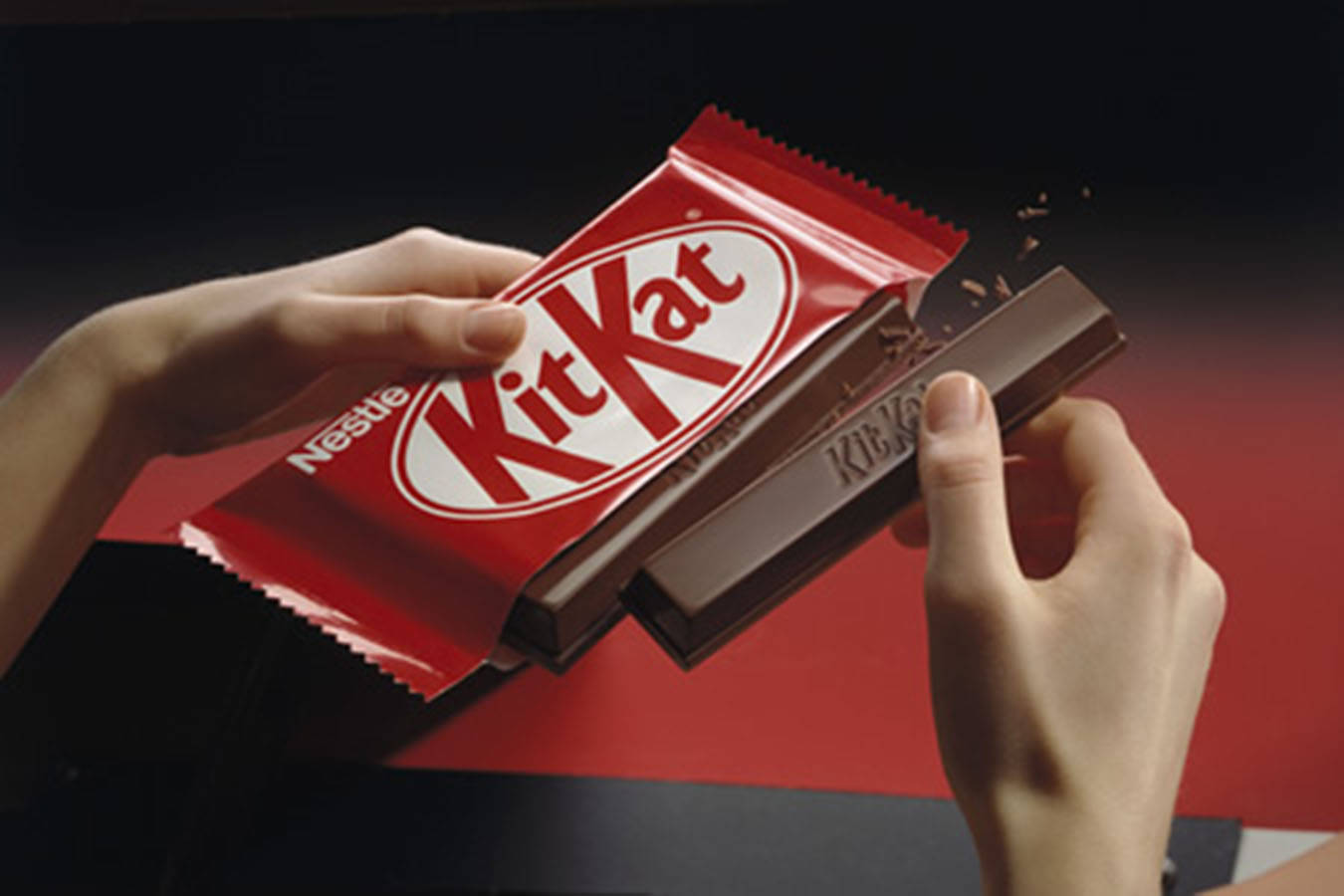 雙手拆開 Kit Kat 巧克力 壁紙 — 雙手撕開紅色KitKat包裝，露出朱古力棒，脆脆的威化層正在碎裂。