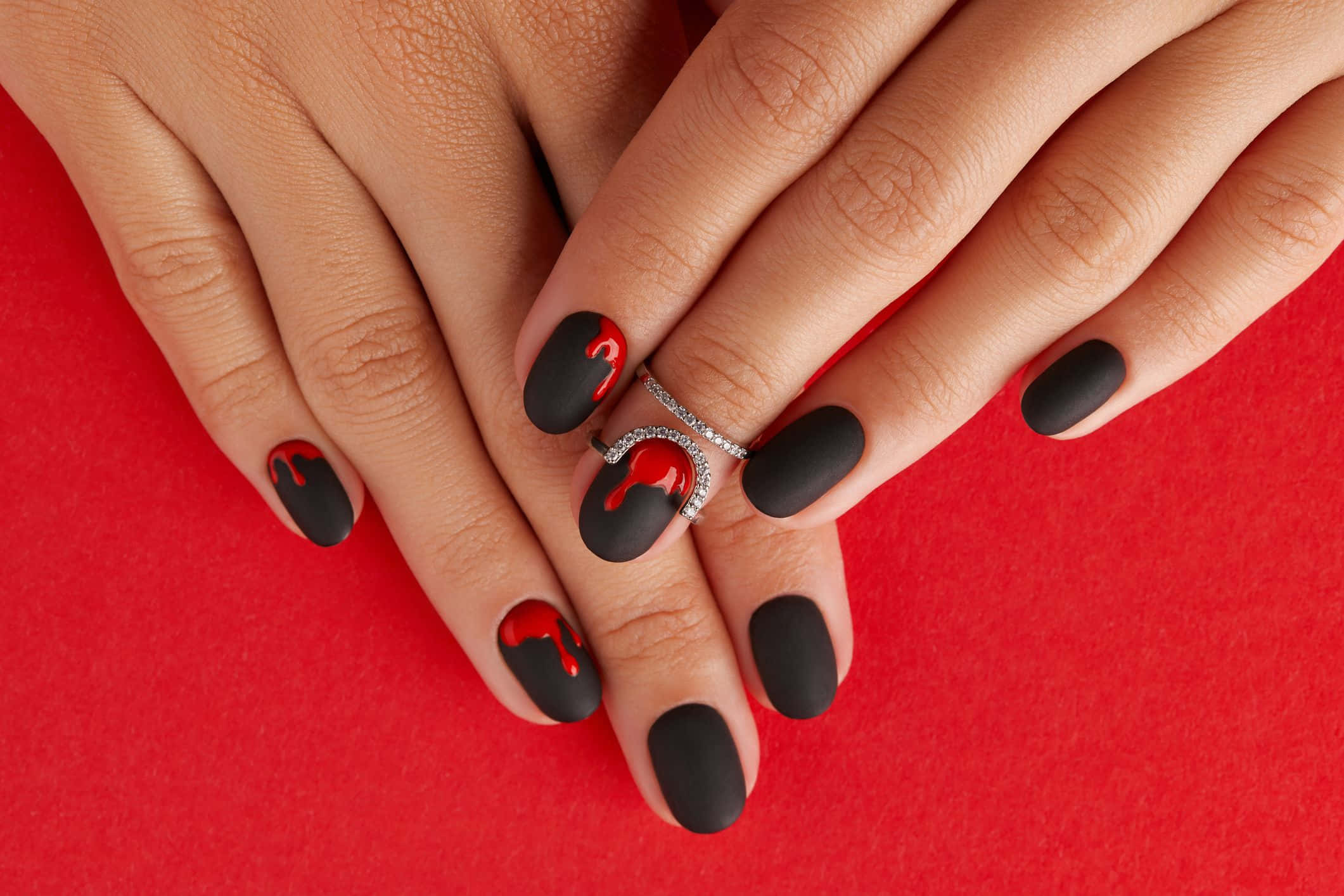 Halloween Nail Art 桌布 壁紙 — 雙手特寫，啞光黑色指甲帶有紅色滴落設計，背景為鮮豔的紅色。