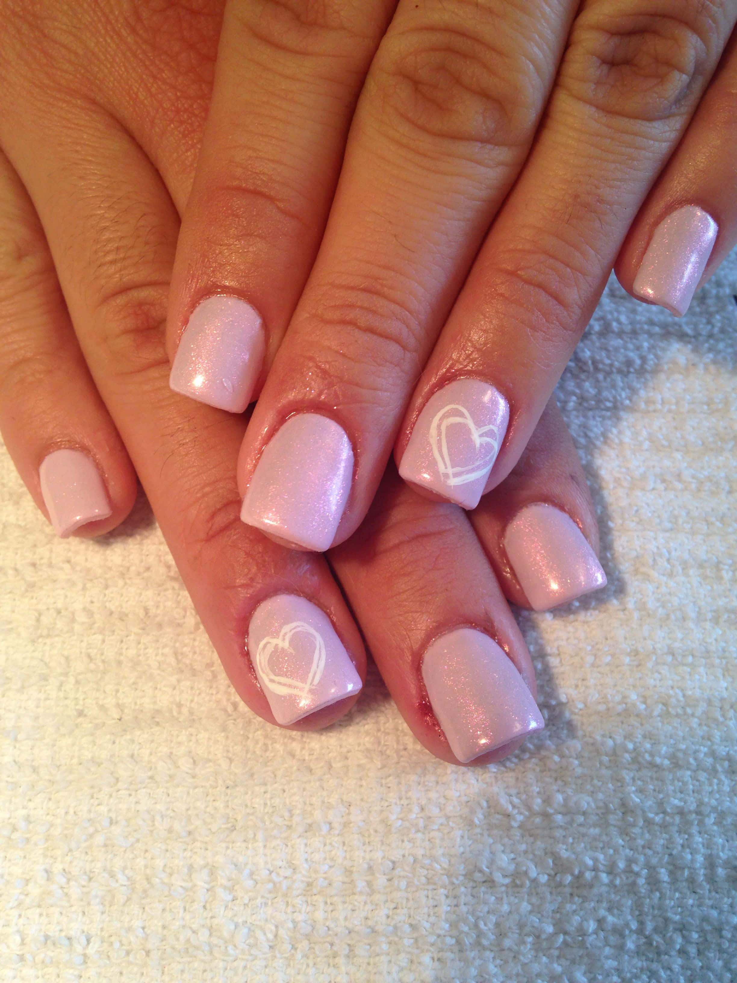 Pink Nail Art 桌布 壁紙 — 雙手特寫，帶有淺粉紅色閃粉指甲和白色心形貼紙，放在有紋理的白色毛巾上。
