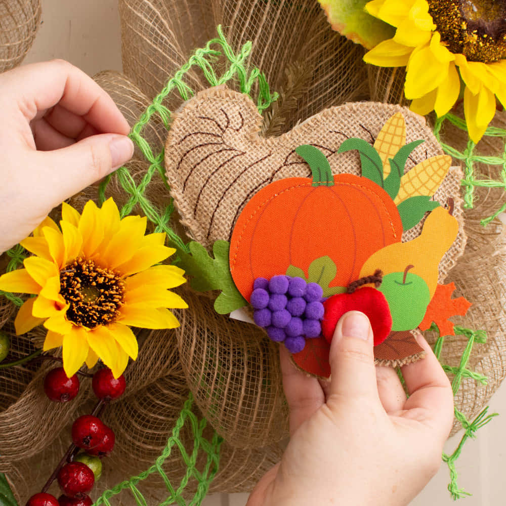 Fall Cornucopia 桌布 壁紙 — 雙手用麻布、向日葵、南瓜和漿果組裝一個質樸的秋季花環。