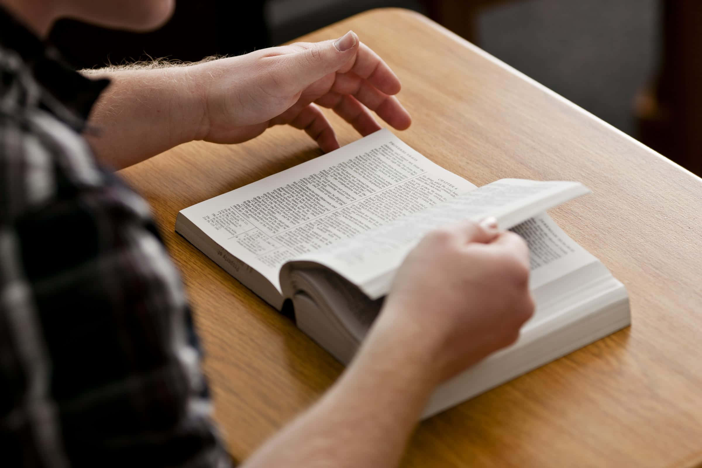 Bible Study 桌布 壁紙 — 雙手翻開放在木桌上嘅書本頁面嘅特寫。