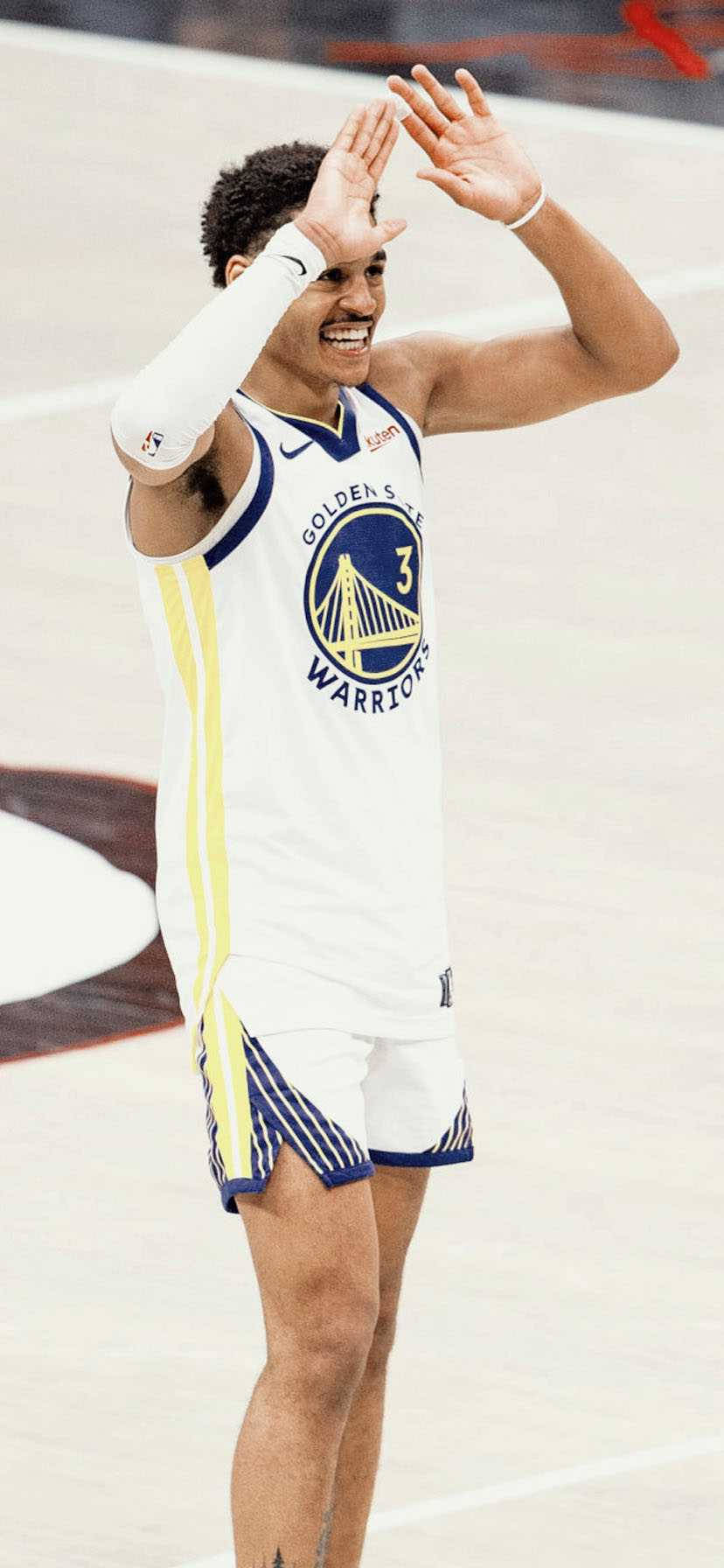 雙手舉起的Jordan Poole 壁紙 — 一位身穿白色球衣的金州勇士籃球運動員在光滑的球場上微笑並向球迷揮手。