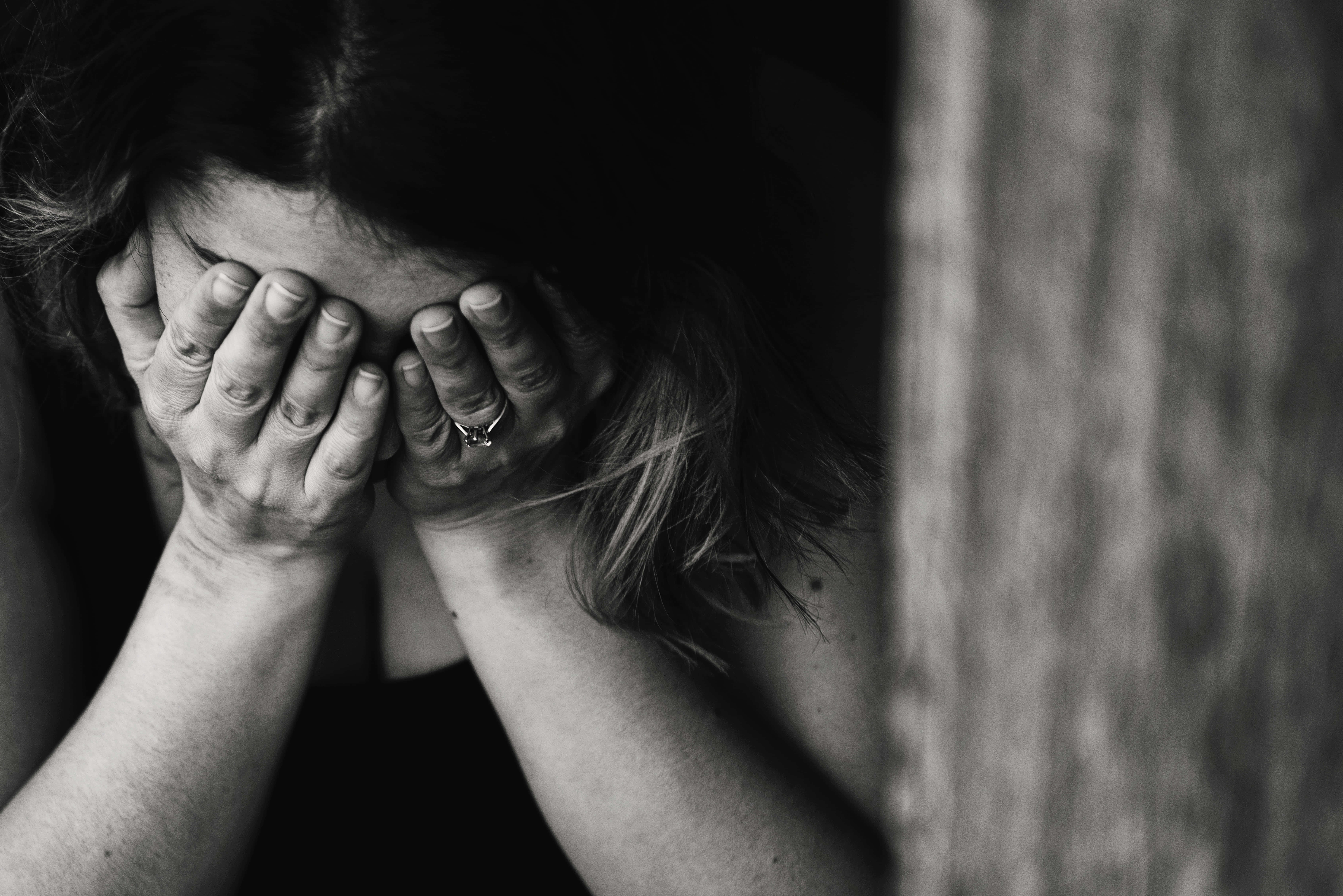 雙手覆面的憂鬱女子圖 壁紙 — 一個黑白的人喺木頭表面旁邊用雙手遮住臉，處於深深嘅痛苦時刻。