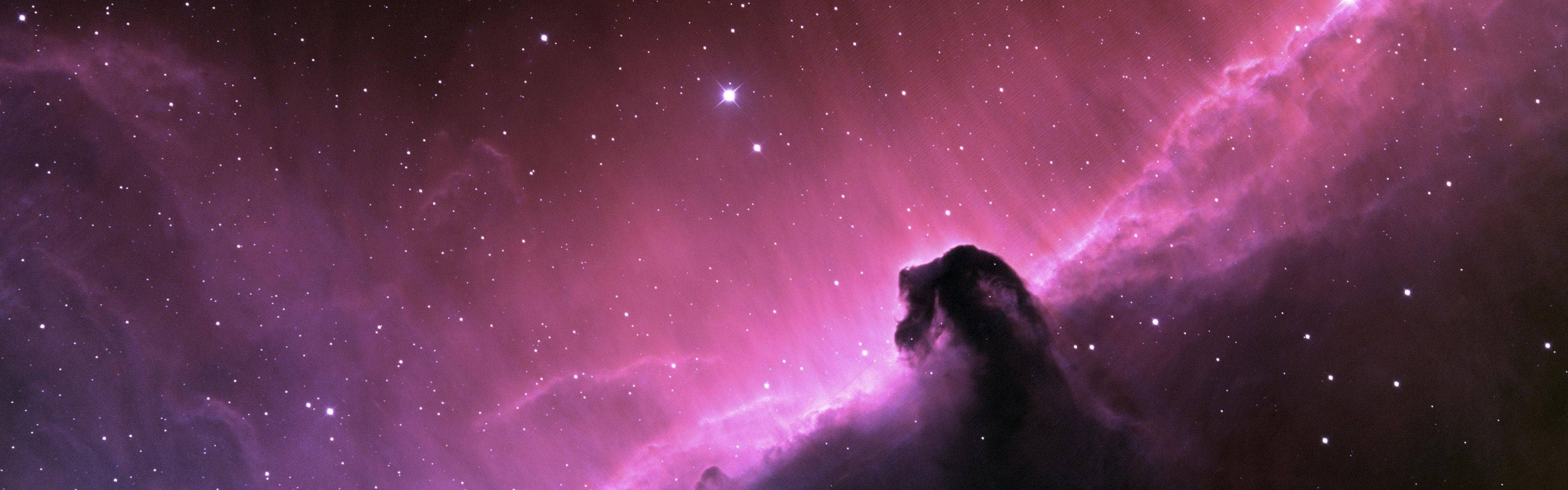 一個粉紅色和紫色的星雲，帶有黑暗的宇宙輪廓，襯托著星空。
