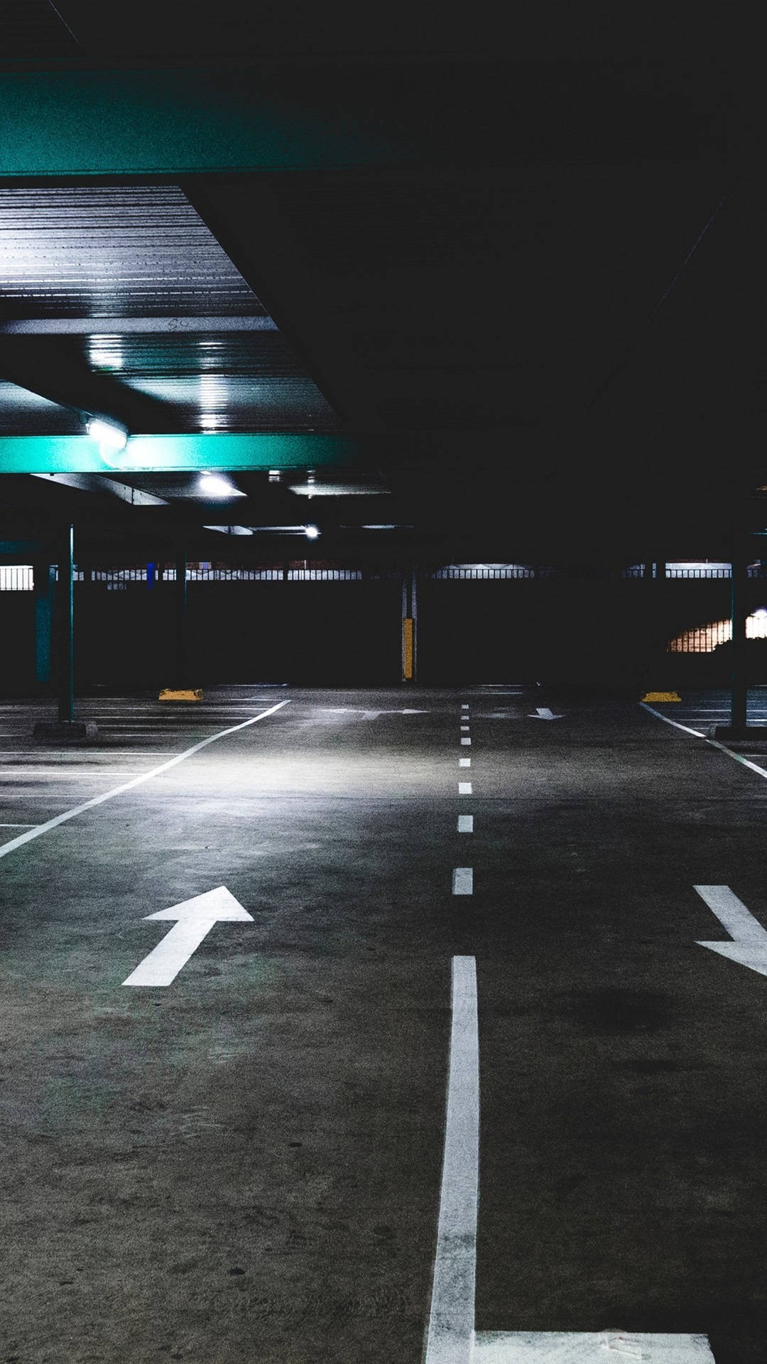 雙車道地下停車場 壁紙 — 燈光昏暗的地下停車場，帶有鮮明的白色方向箭頭和發出綠色光芒的天花板燈，投下長長的影子。