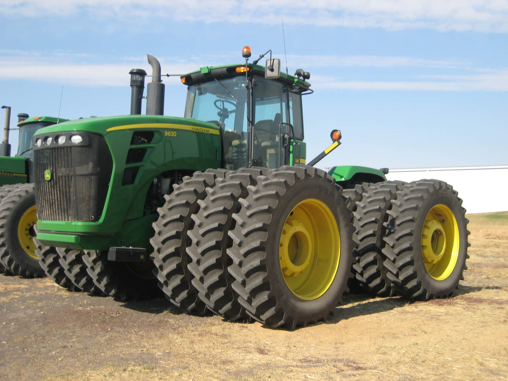 雙輪拖拉機圖片 壁紙 — 一部綠色和黃色的John Deere 9630拖拉機配備巨大輪胎，停放在乾燥的土地上，天空清澈湛藍。