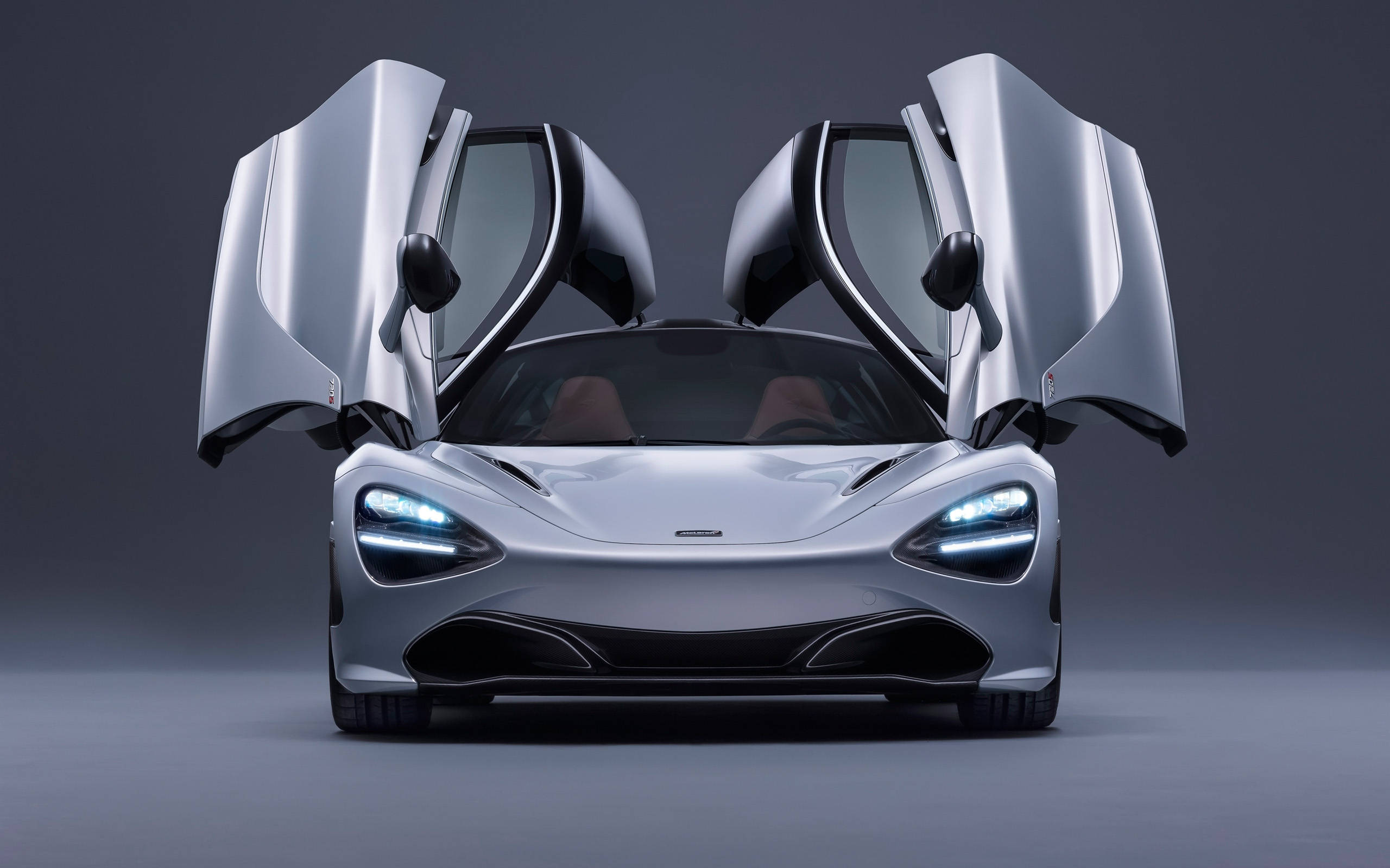 雙門開啟的麥拉倫720S 壁紙 — 一架流線型銀色McLaren跑車，鷗翼車門打開，以深灰色工作室背景襯托。