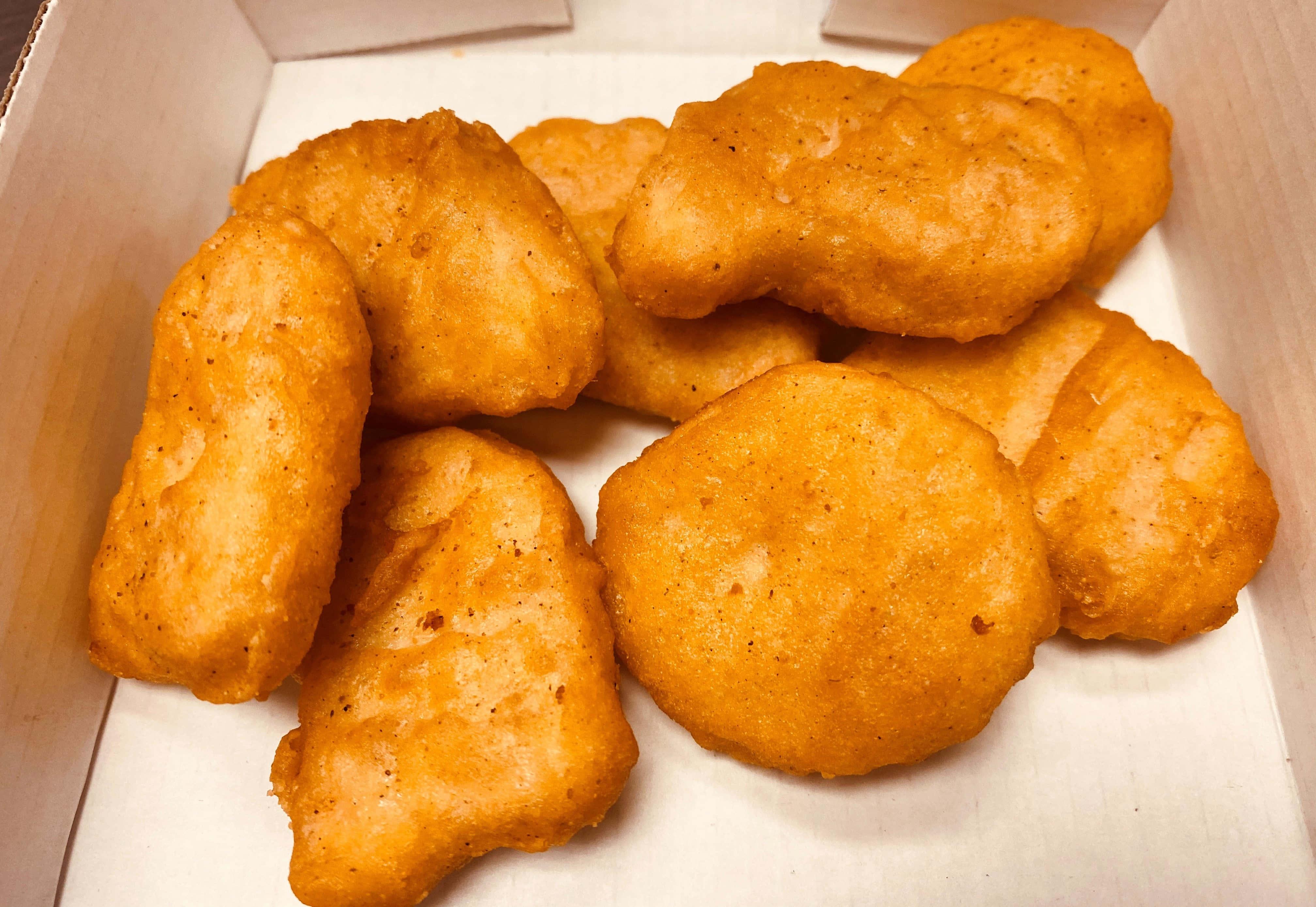 雞塊簡單照片 壁紙 — 金黃色炸雞塊堆疊在白色紙板盒中，帶有酥脆的麵包糠外層。