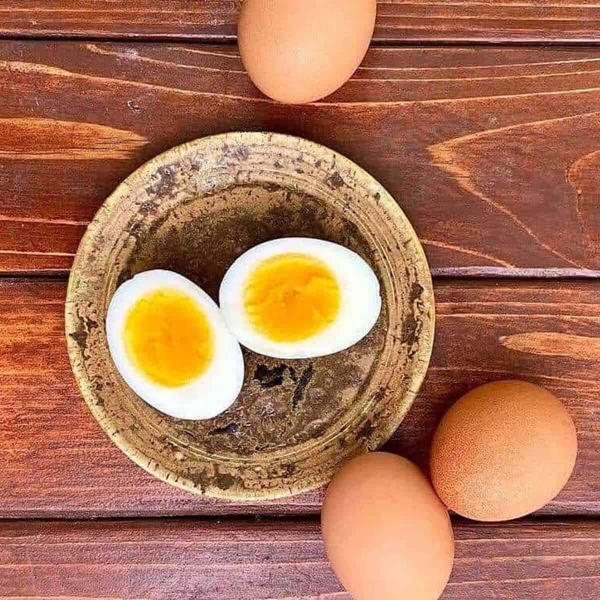 雞蛋的獨特視角 壁紙 — 兩個切半的水煮蛋，蛋黃鮮豔，放在一個質樸的碗裡，置於木質表面上，周圍環繞著完整的雞蛋。