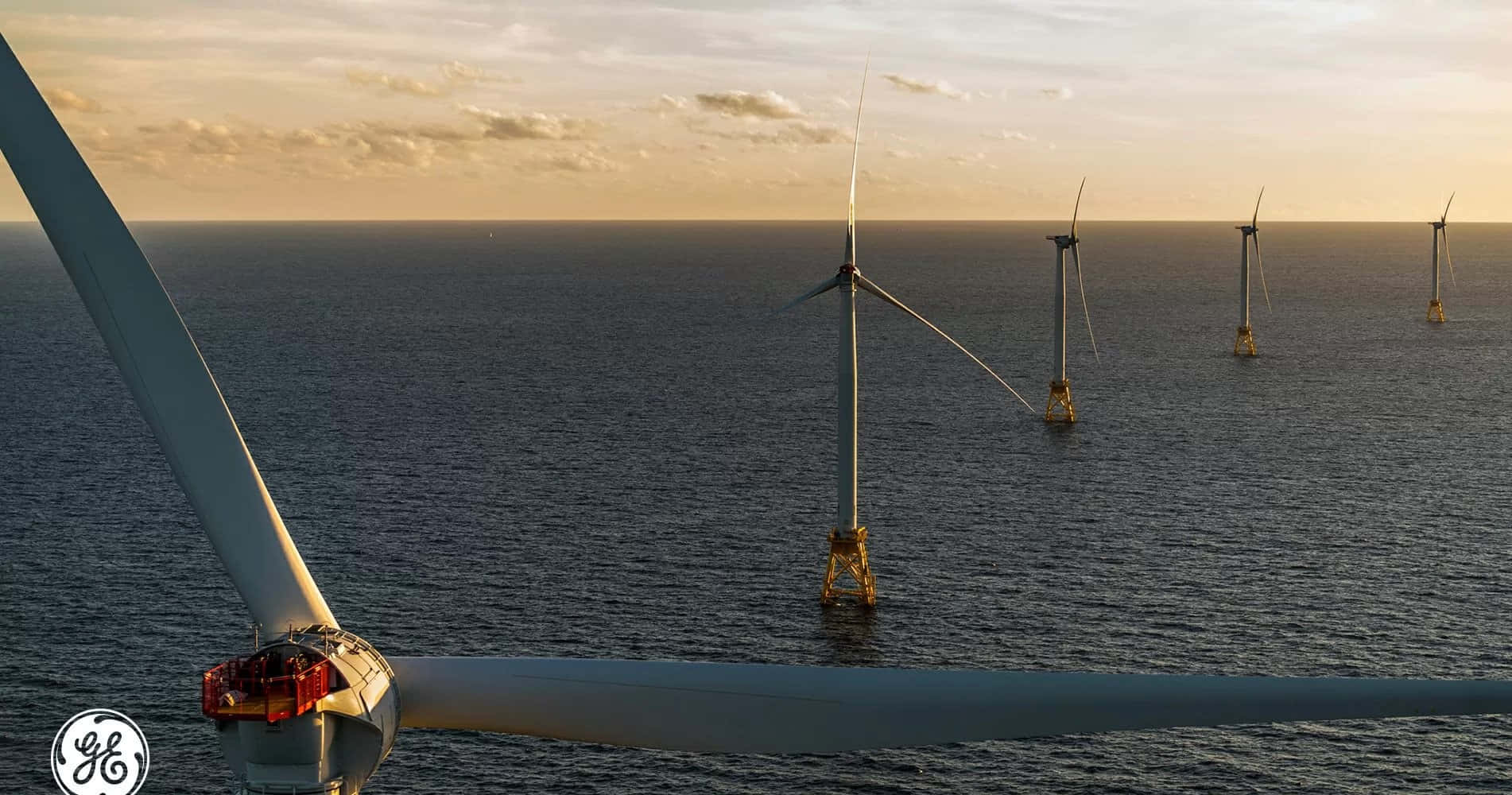 Wind 桌布 壁紙 — 離岸風力發電機在平靜的海面上，沐浴在金色的日落天空下。