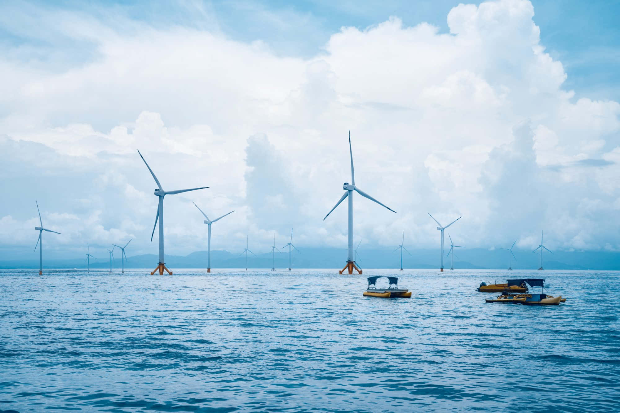 Wind 桌布 壁紙 — 離岸風力發電機在平靜的藍色海水中高聳，天空部分多雲，附近有小船。