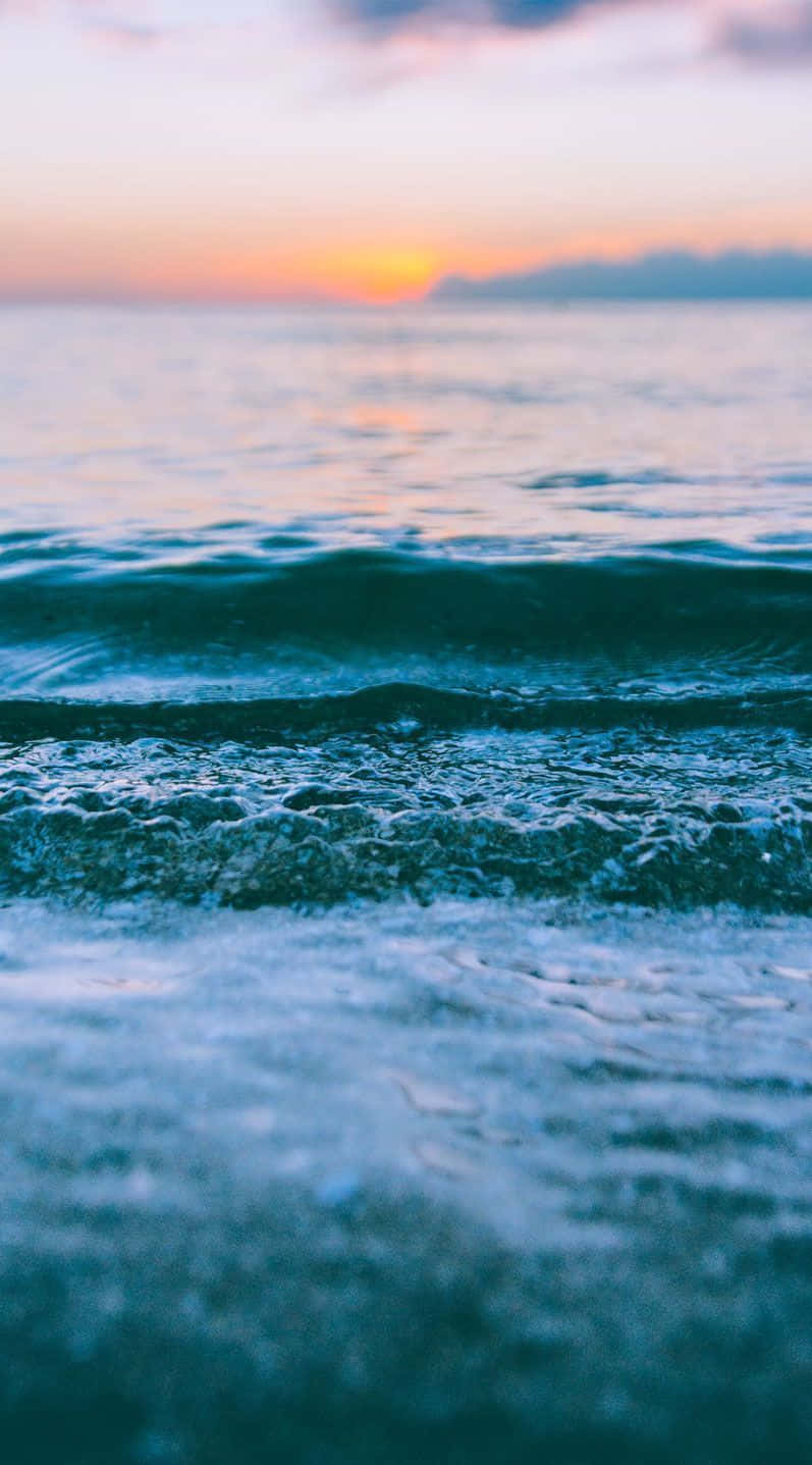 難以置信的日落海灘美景 壁紙 — 夕陽將海洋染成溫暖的橙色和清涼的藍色，溫柔的海浪向岸邊翻滾。