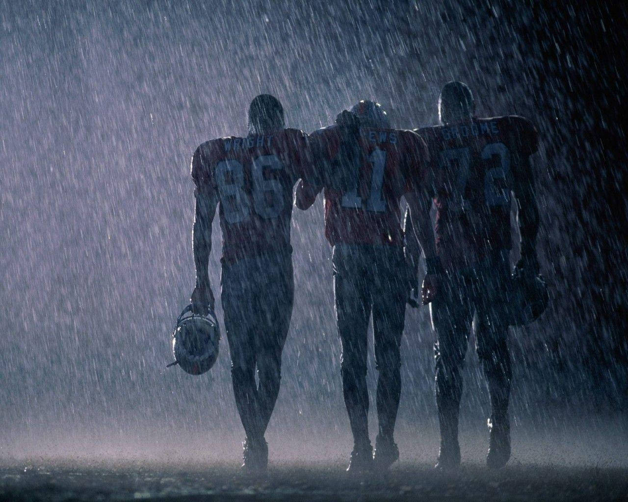 雨中NFL美式足球運動員 壁紙 — 三名身穿紅色球衣的足球員手持頭盔在暴雨中走遠。